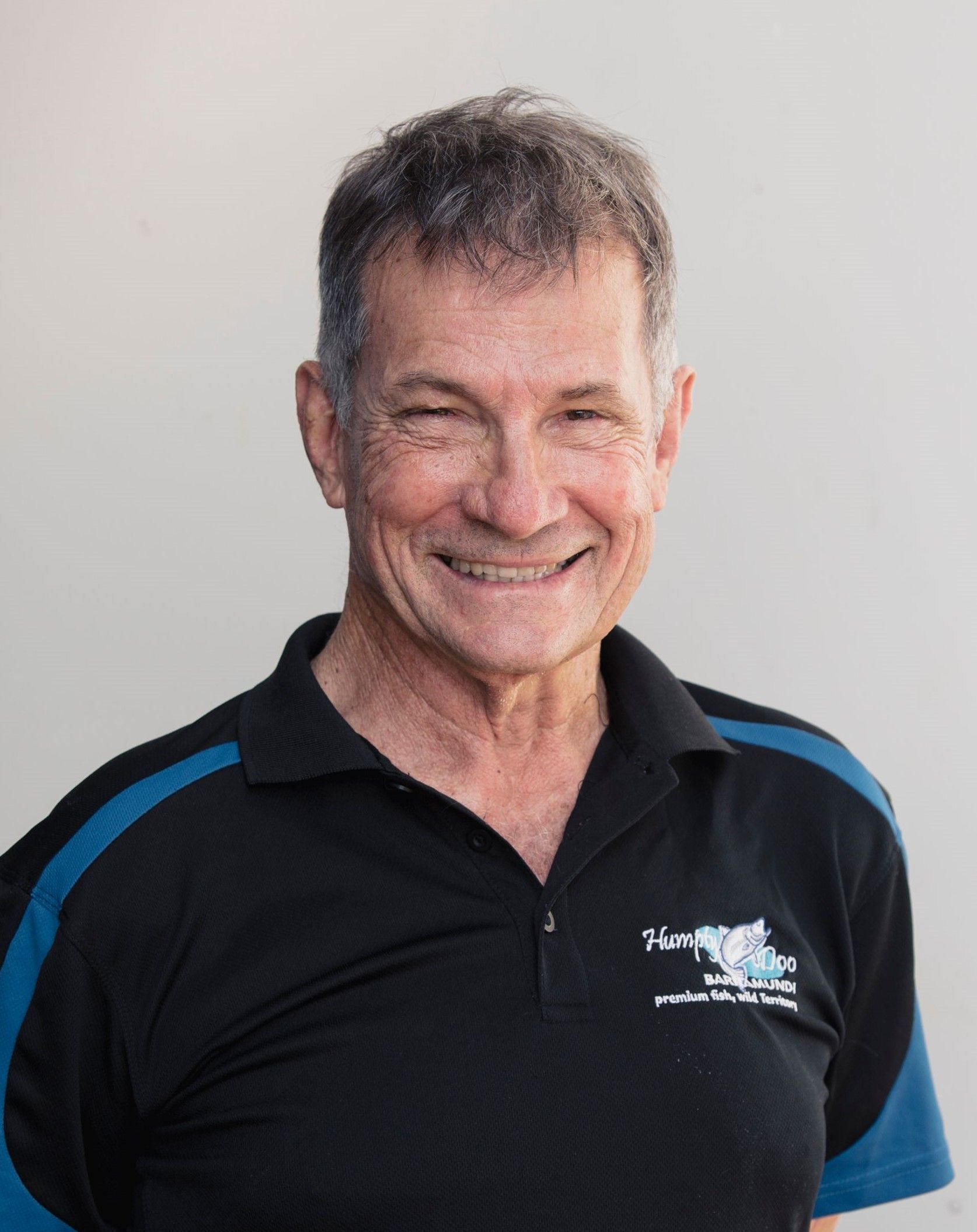 Smiling person wearing a black polo shirt with teal accents against a plain background.