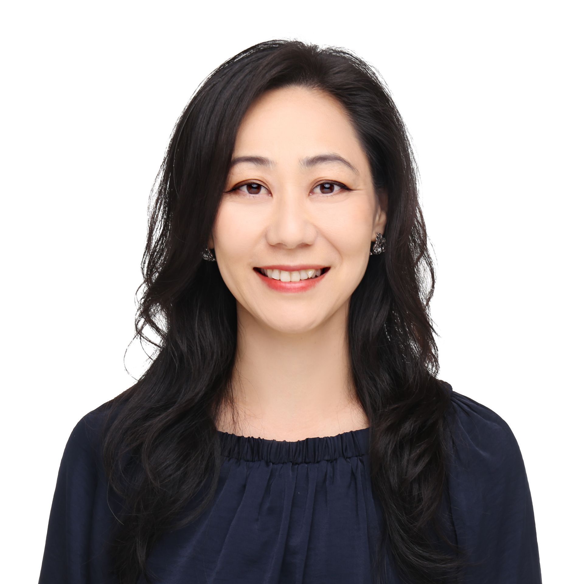 A professional headshot of a smiling person with dark, wavy hair, wearing a dark blue top against a white background.
