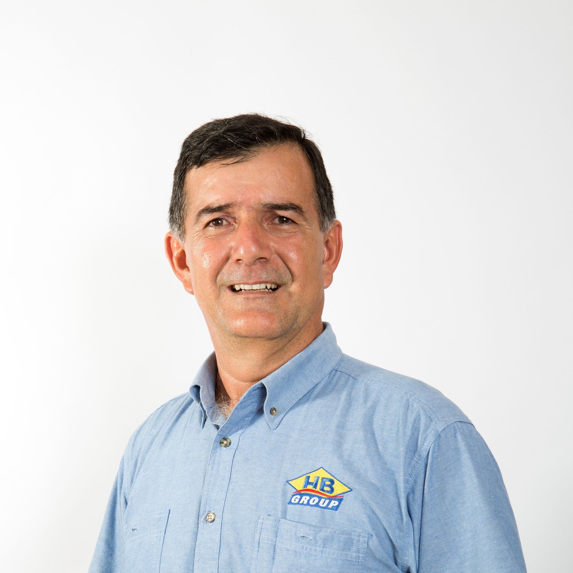 A person with short dark hair smiling, wearing a blue button-down shirt with a WB Group logo, set against a white backdrop.