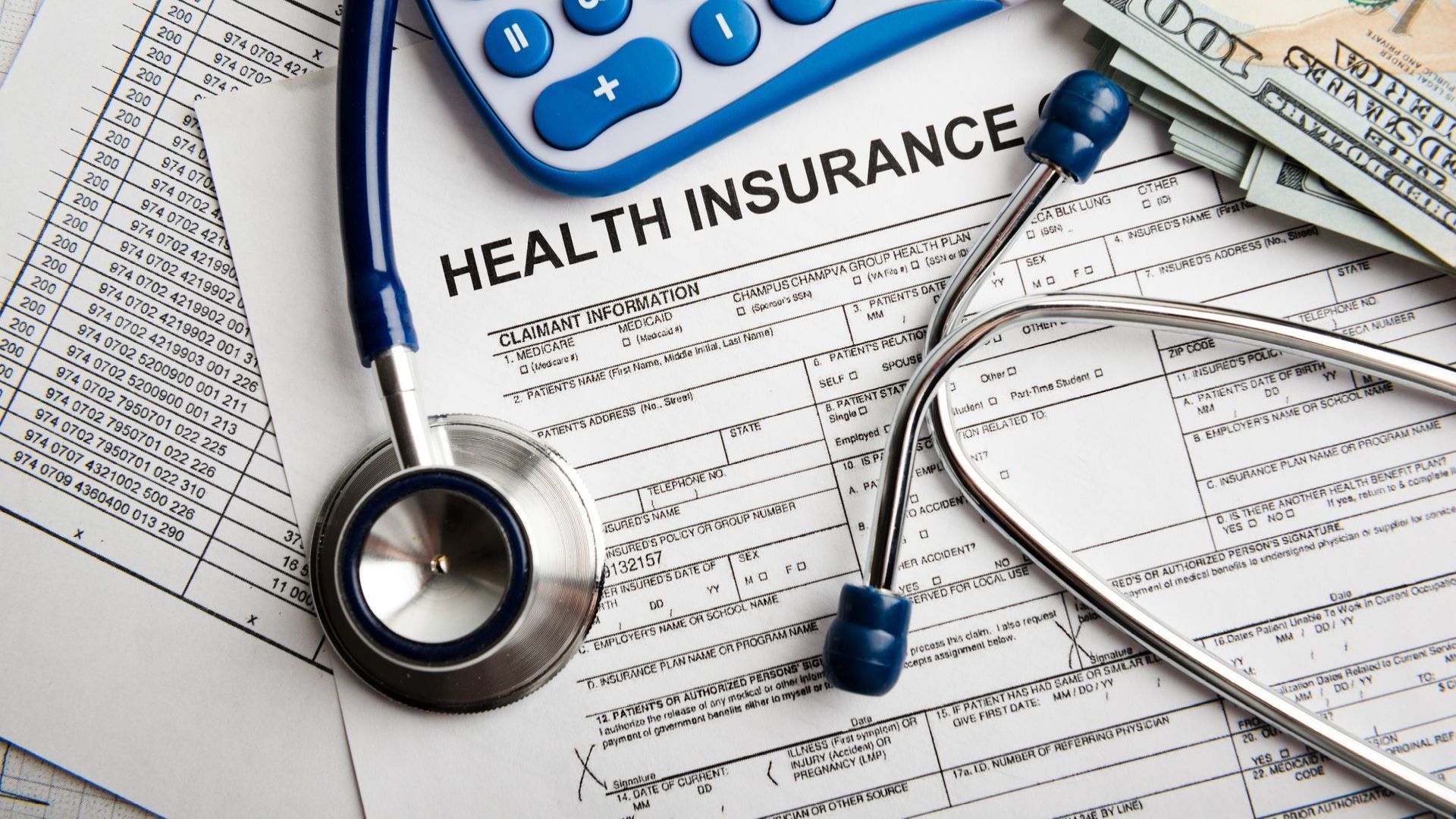 a stethoscope , calculator , and money are on top of a health insurance form .