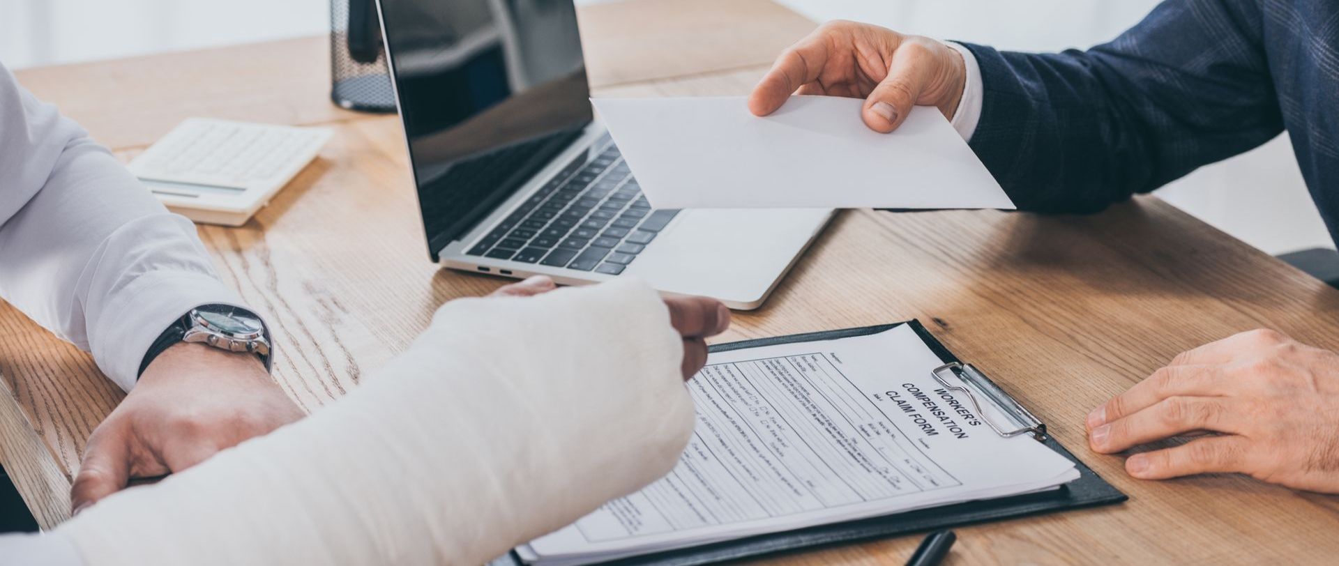 a man with a cast on his arm is sitting at a table with a laptop and a clipboard .