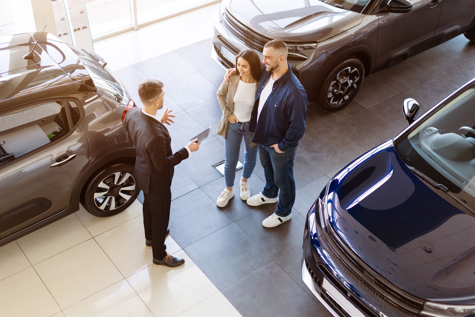 Car salesperson showing a tablet to a couple in a car showroom; cars in the background.
