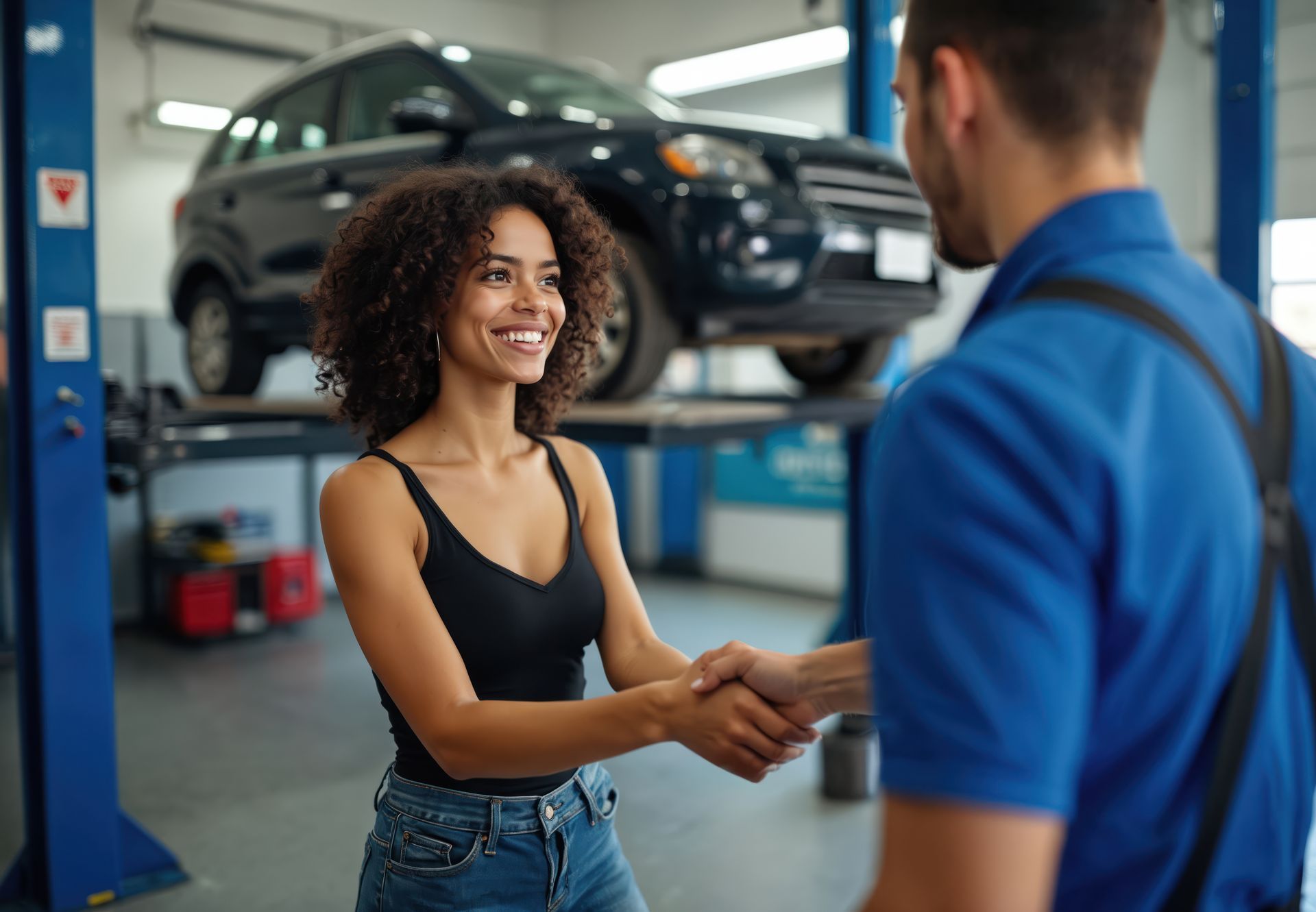 Woman shaking hands with mechanic in a car repair shop; car on a lift in background.