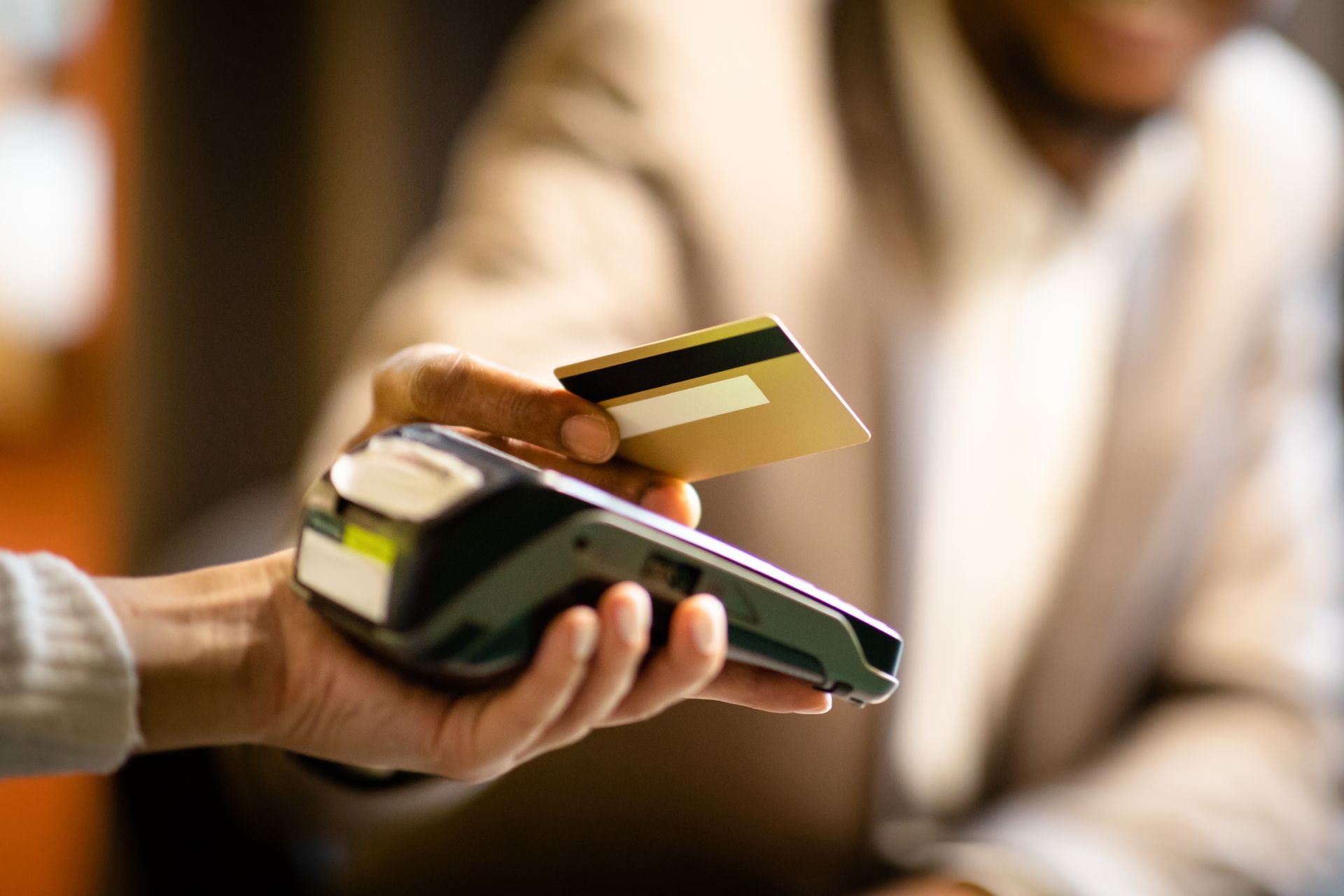 Person paying with a credit card at a payment terminal; close-up of card and hand.