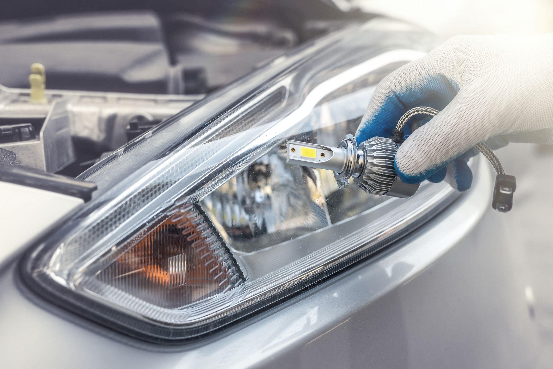 Person in a glove is installing a new LED headlight bulb in a car headlight.