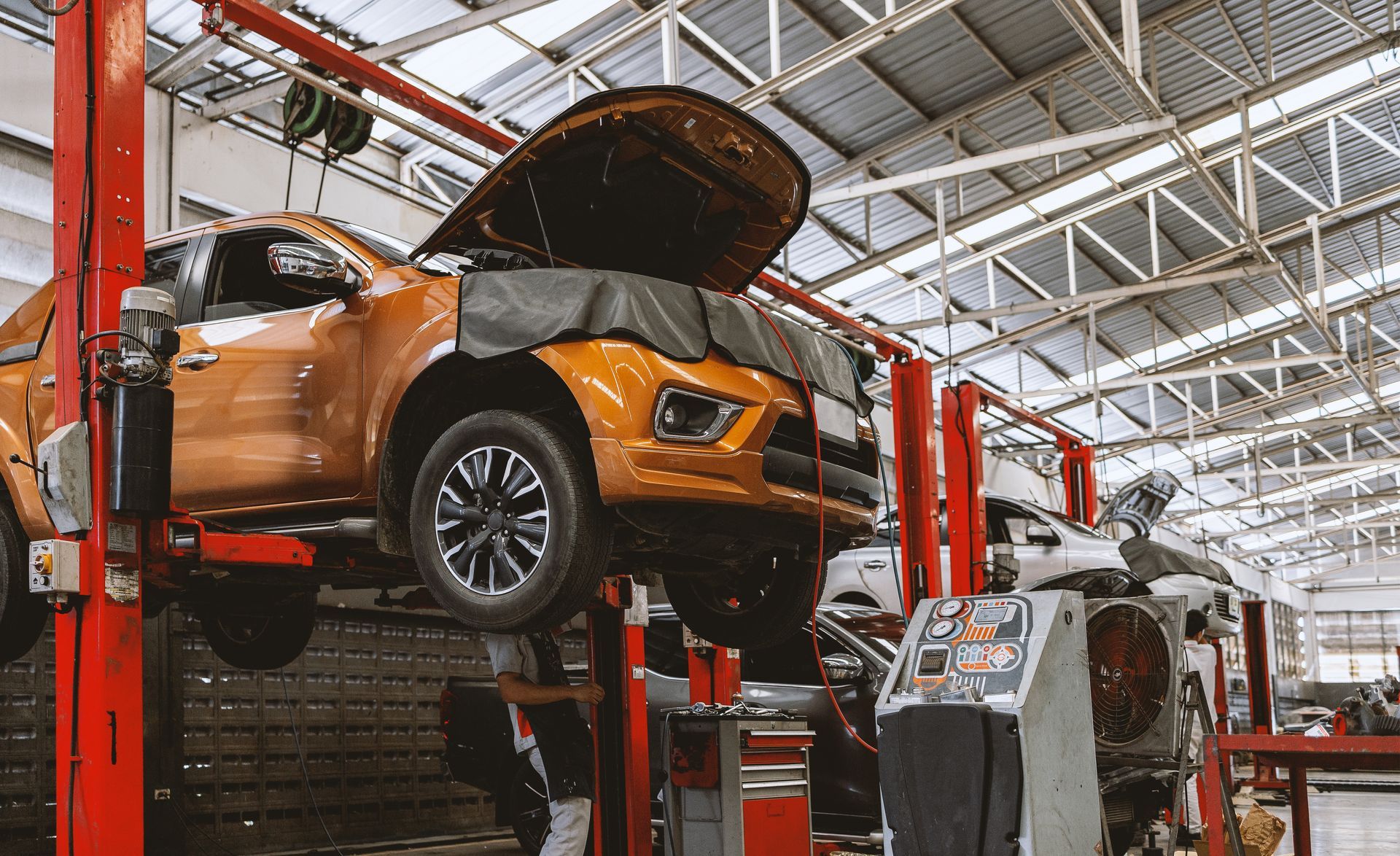 Orange truck on a lift in a repair shop with the hood open.