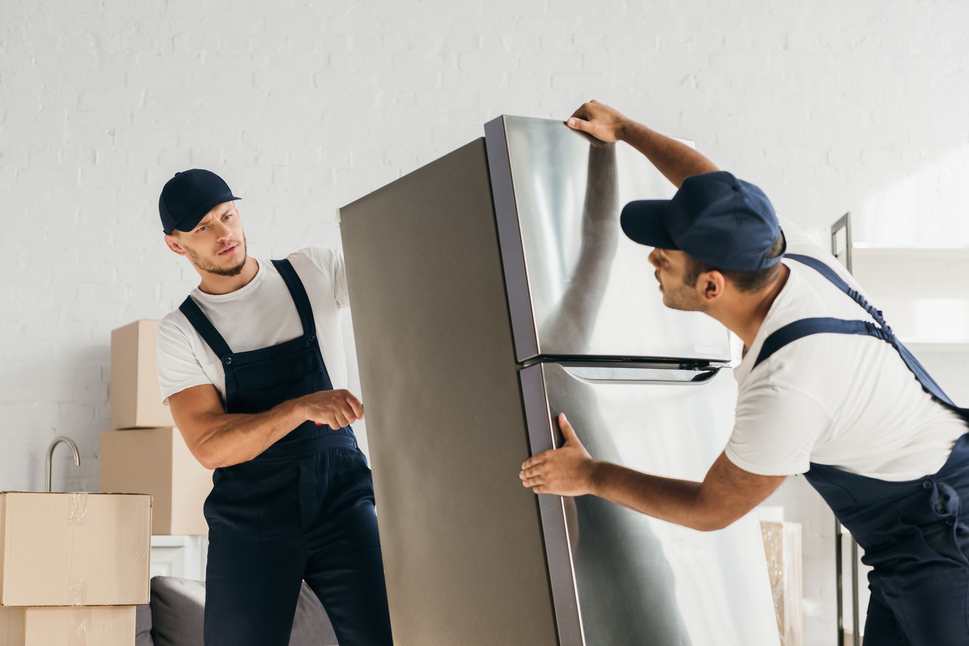 Two movers lifting a refrigerator in a room with cardboard boxes.
