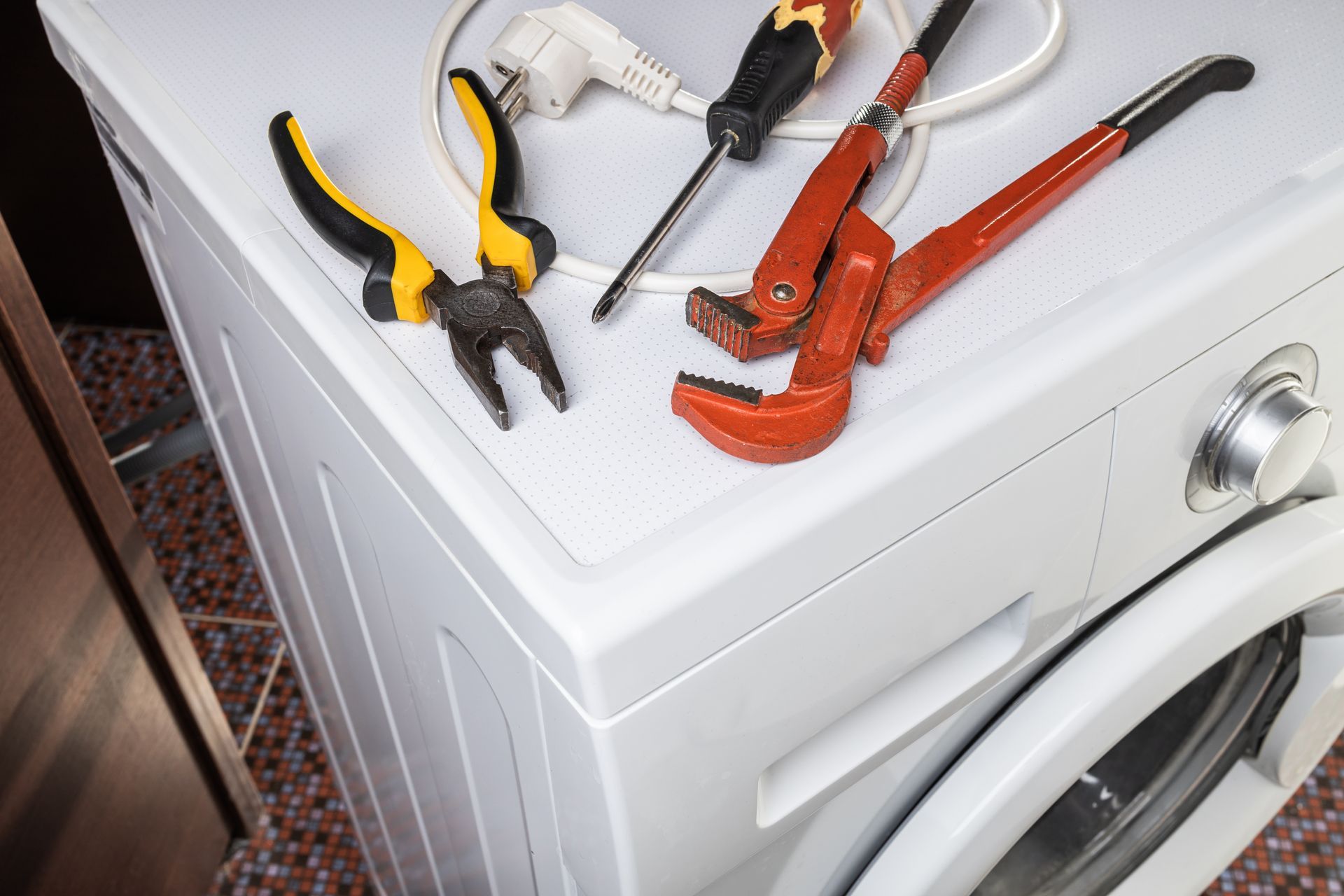 Washing machine with various repair tools, including pliers, screwdriver, and wrench, on top.
