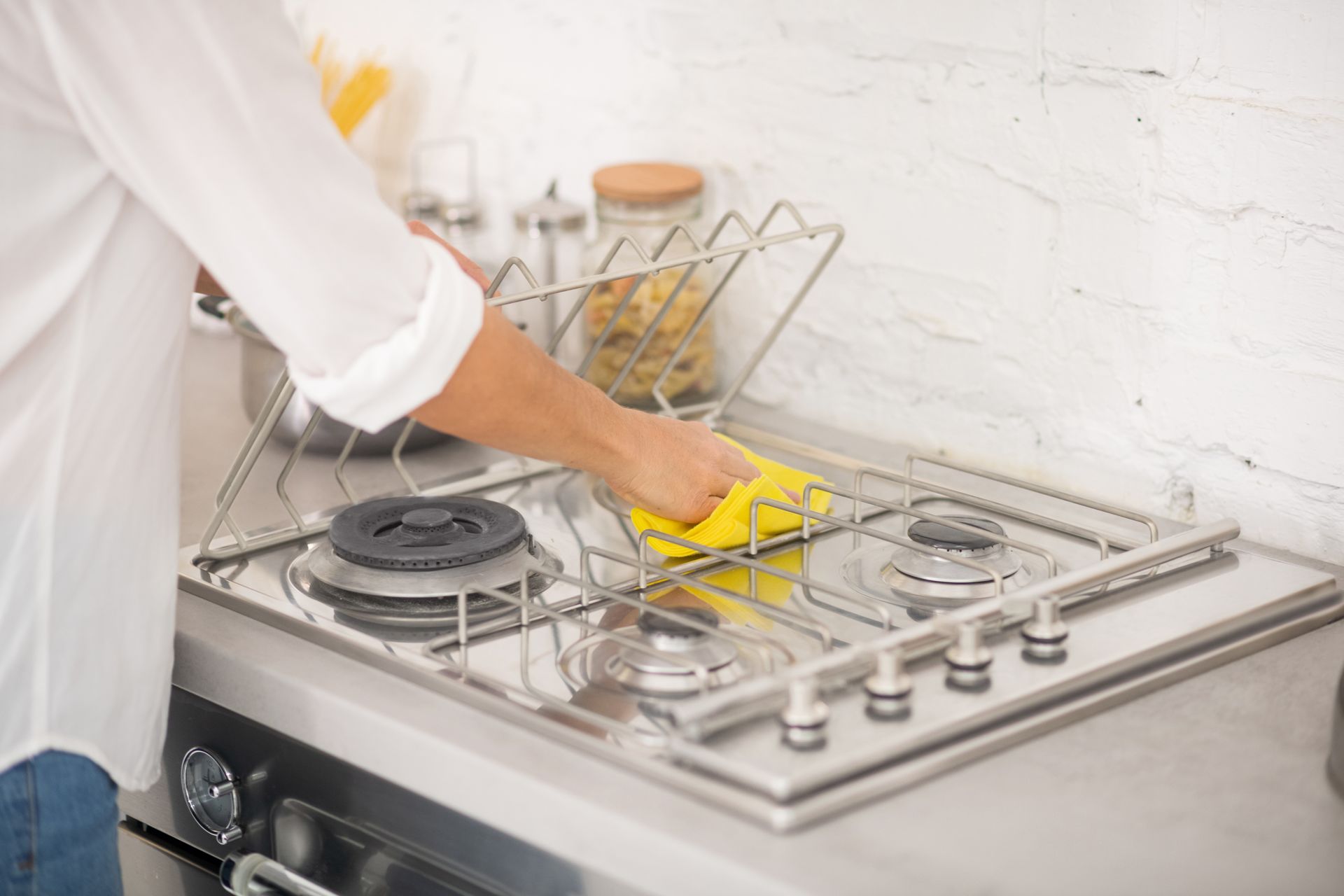 Person cleaning a stainless steel stovetop with a yellow cloth in a kitchen.