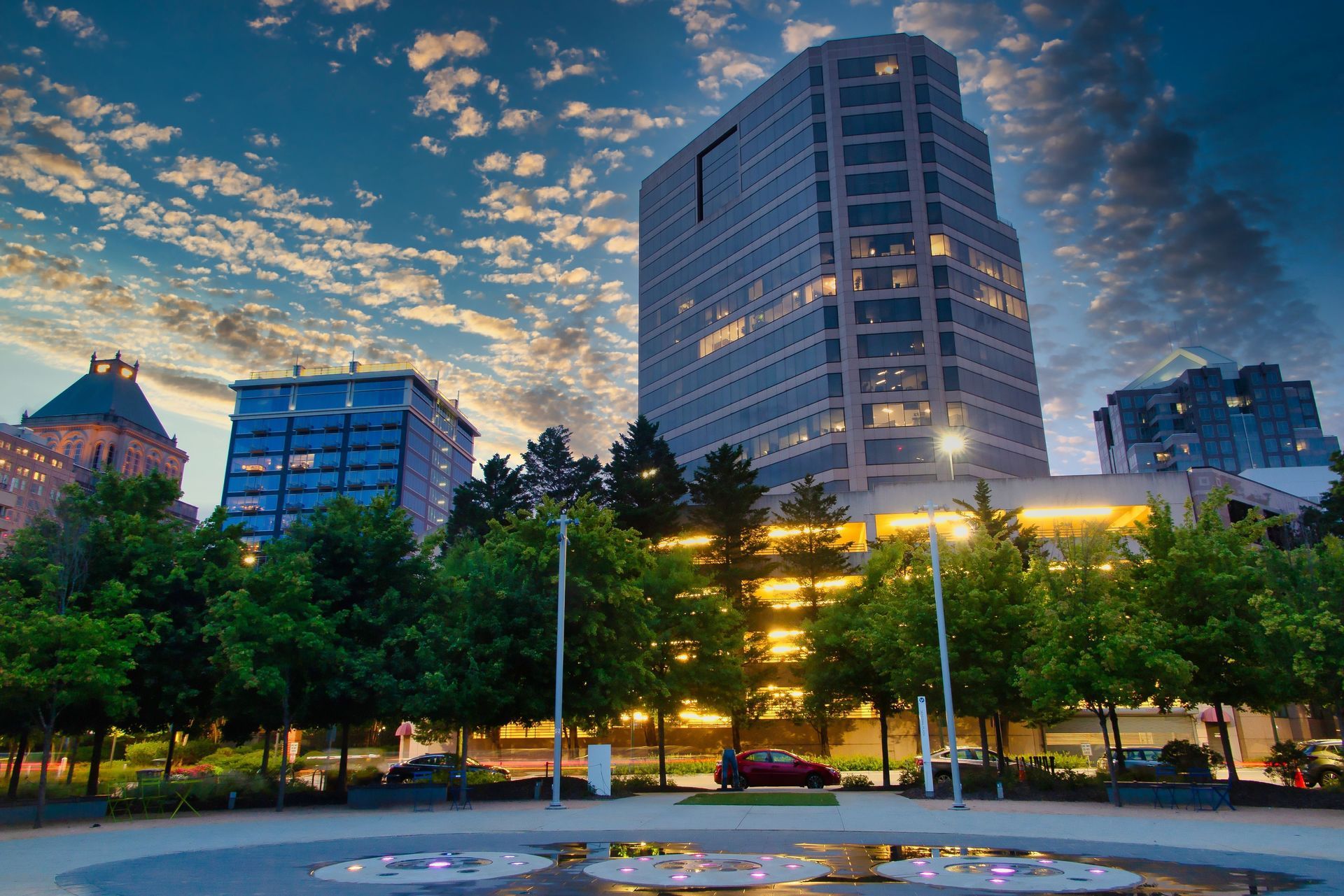 City skyline with tall buildings, trees, and cloudy sky at dusk.