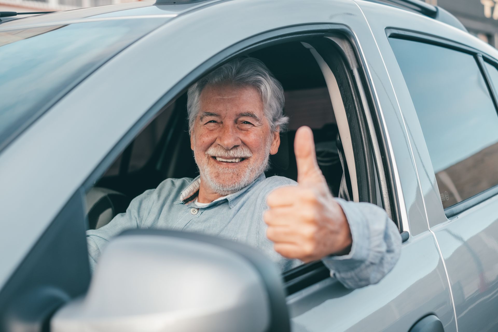 Smiling person in a car giving a thumbs up.