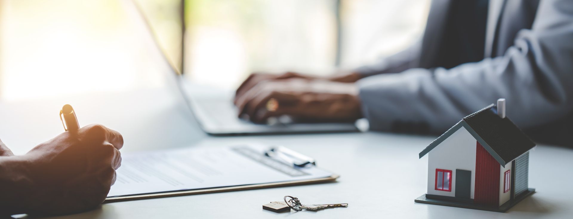 Real estate deal: Signing documents, laptop, model house, keys on table.
