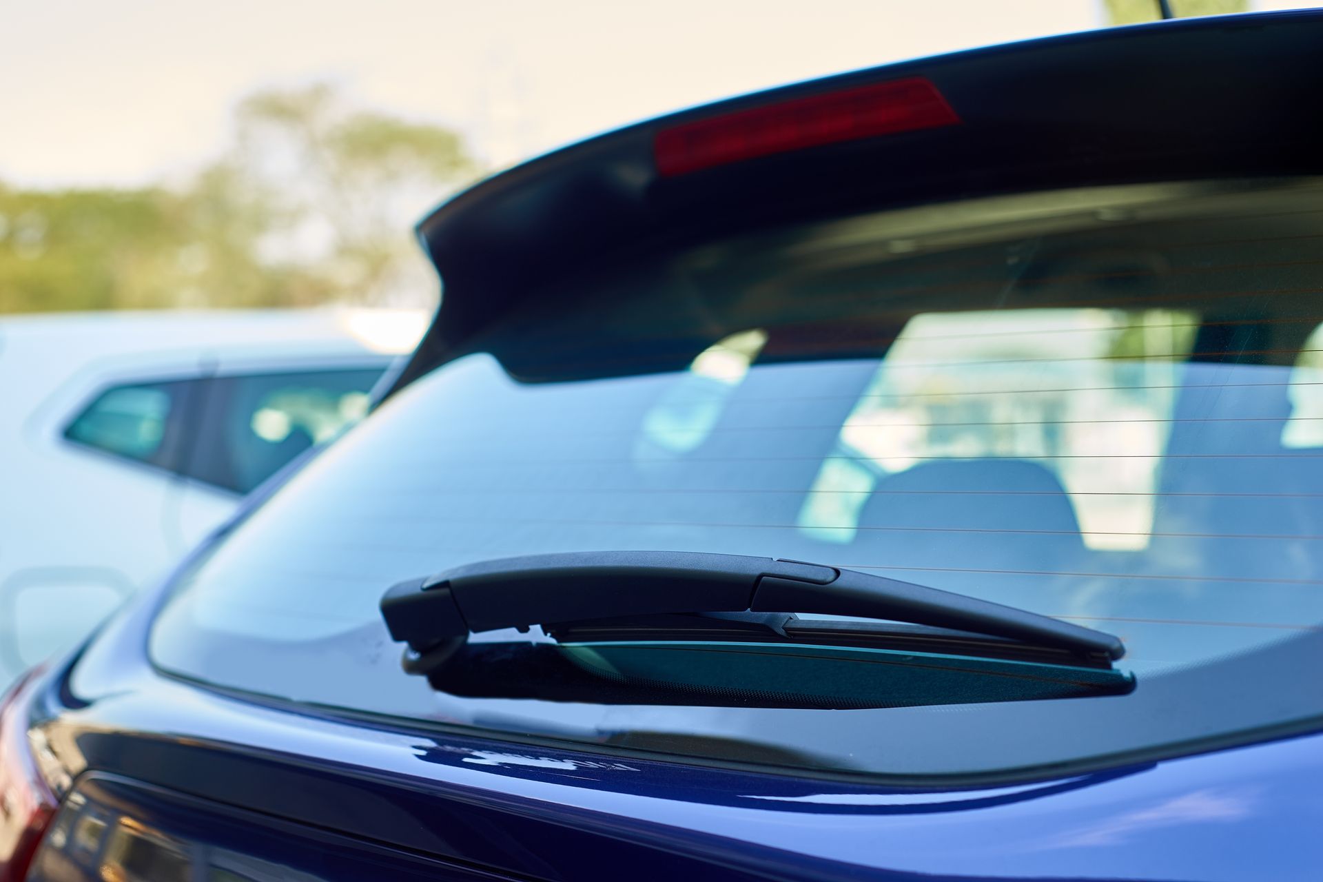 Blue car's rear window with black wiper. Clear glass, blurred background with white car.