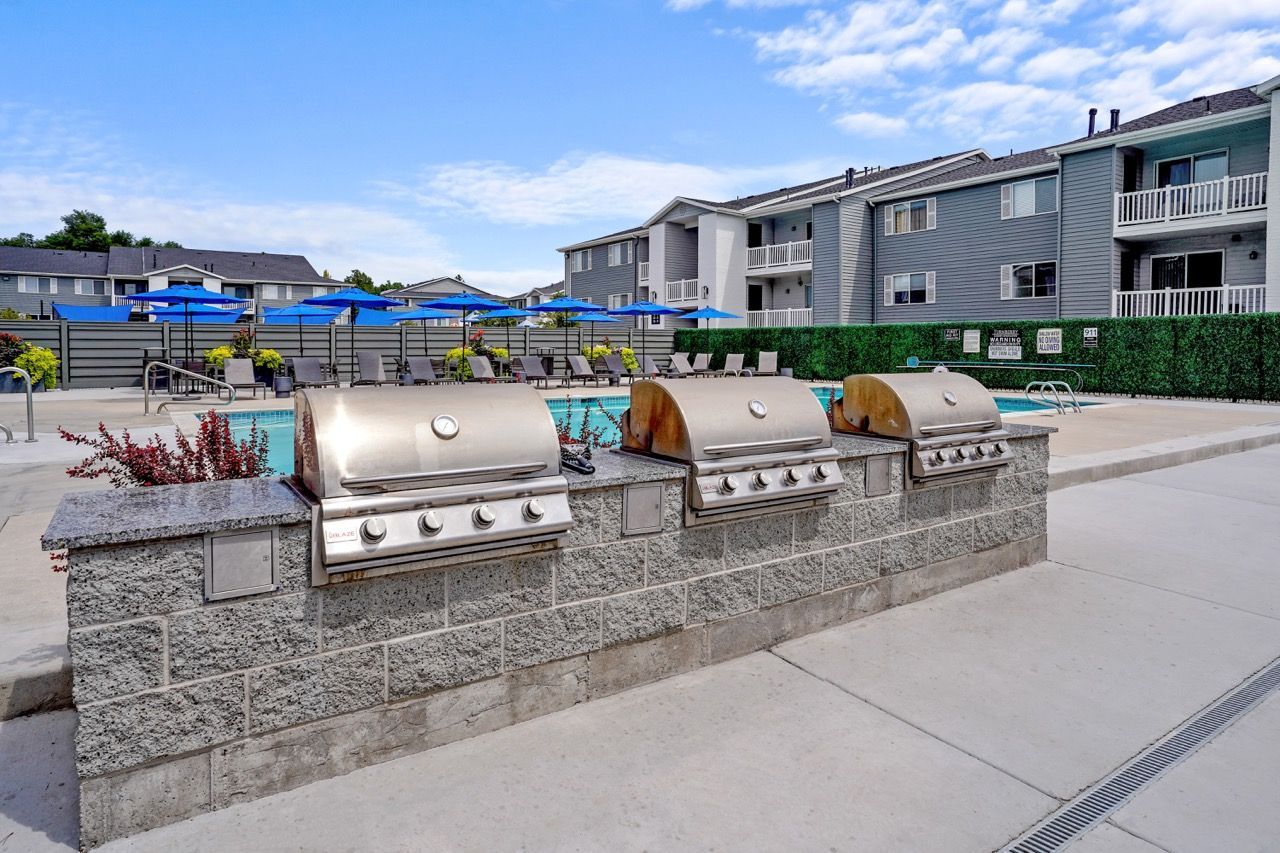 Outdoor community grill station with three built-in grills beside a pool.