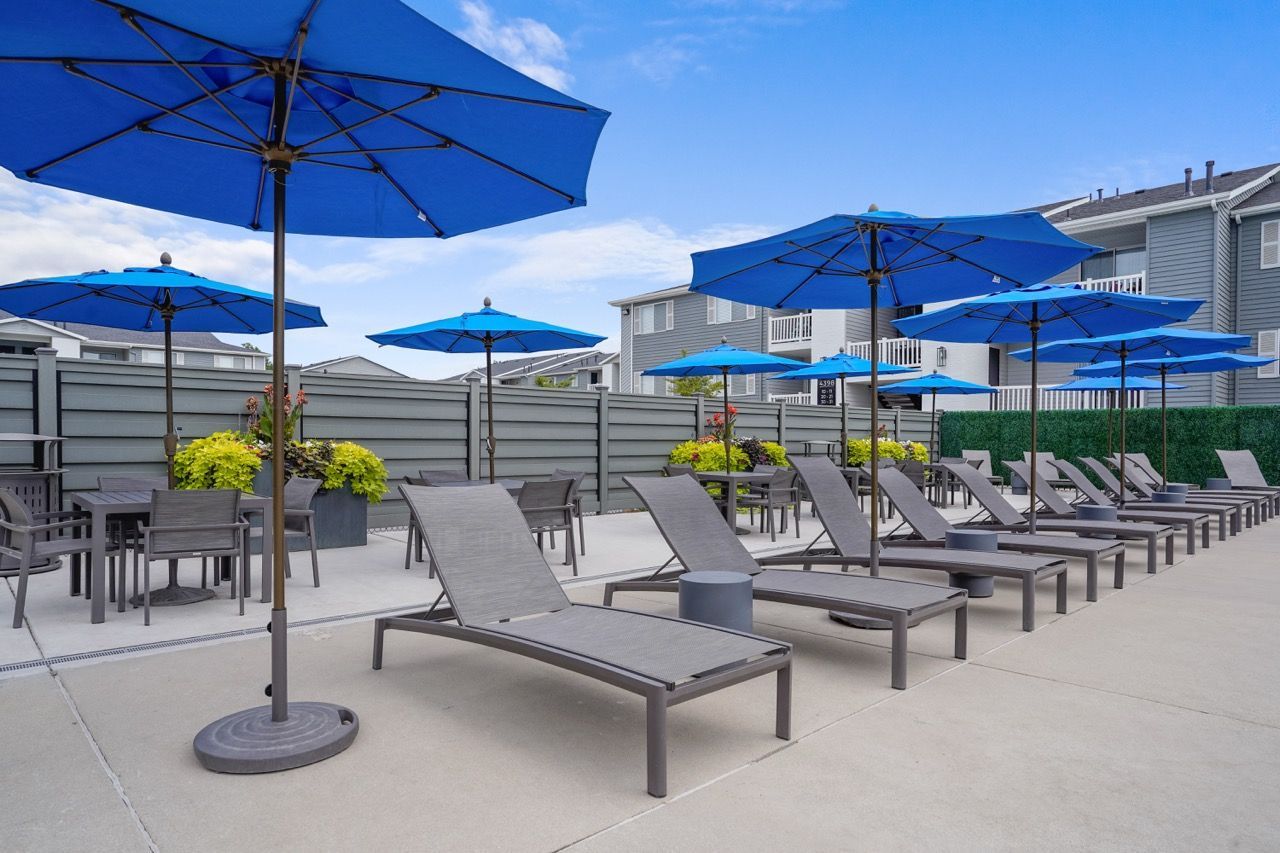 Outdoor community patio with blue umbrellas, lounge chairs, and tables.  Plan a visit to Turnberry Apartments and experience convenient apartments near Downtown Salt Lake City, UT during a personalized tour.
