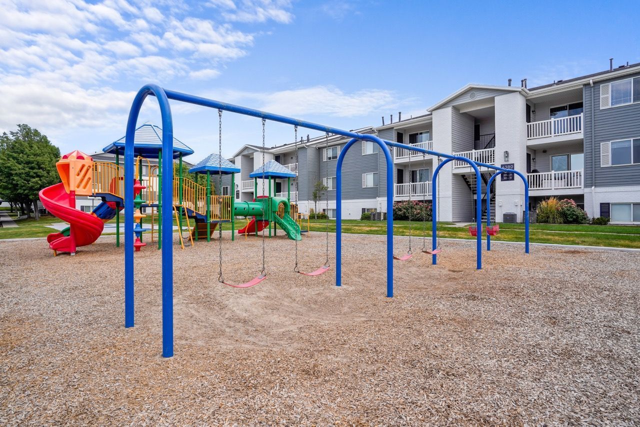 Playground with bright blue swings and colorful play structures in a multifamily community. Stop by Turnberry Apartments to see inviting apartments for rent in Millcreek, UT and experience the community atmosphere.
