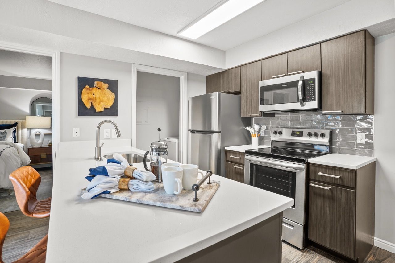 Modern apartment kitchen with stainless steel appliances, dark wood cabinets, and a white island. Experience the comfort of luxury apartments in Millcreek, UT, when you visit Turnberry Apartments for a guided tour.
