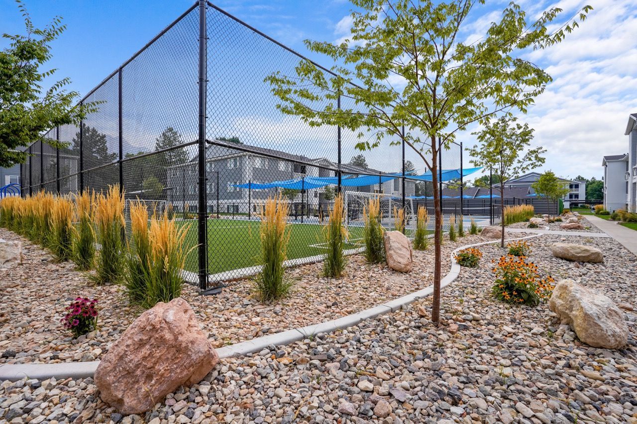 Fenced outdoor recreation court with blue shade sails and surrounding xeriscape landscaping.  Visit Turnberry Apartments to experience thoughtfully designed apartments in Millcreek, UT, during a convenient tour.

