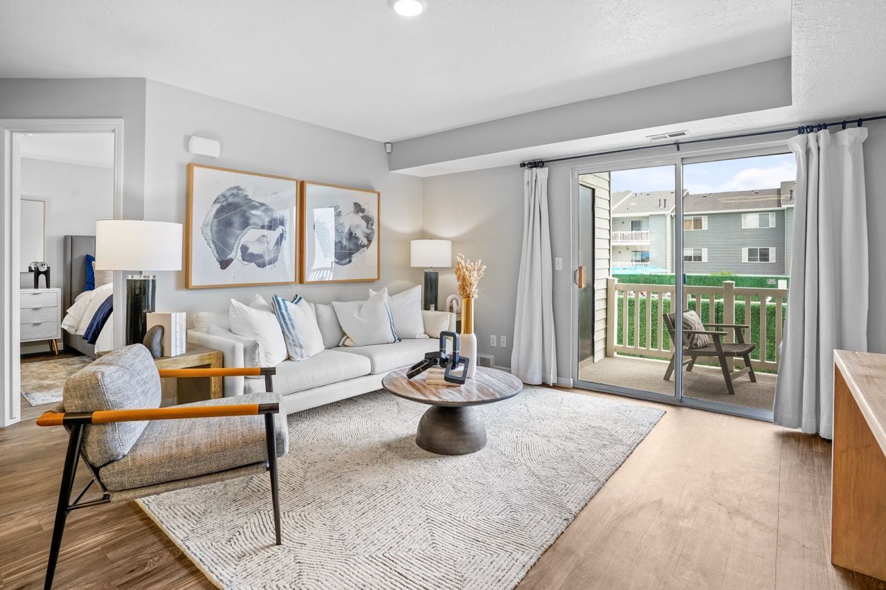 Bright living room with white sofa, armchair, coffee table, and sliding glass door to balcony.  Experience comfortable apartment living in Millcreek, UT, when you explore Turnberry Apartments during a tour.
