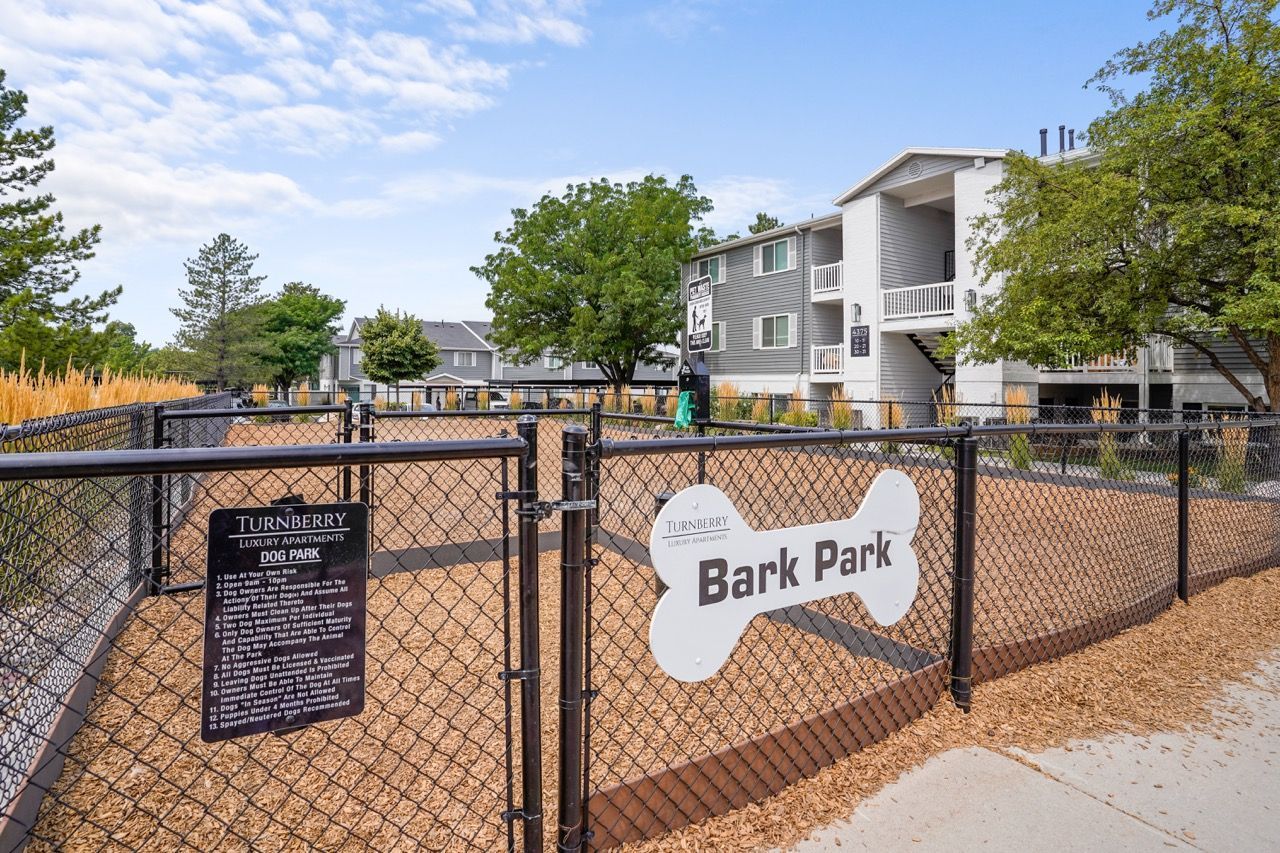 Exterior view of a fenced dog park area at Turnberry Luxury Apartments, with a large Bark Park sign. Take a closer look at our 1, 2 & 3 bedroom apartments in Millcreek, UT by touring Turnberry Apartments.
