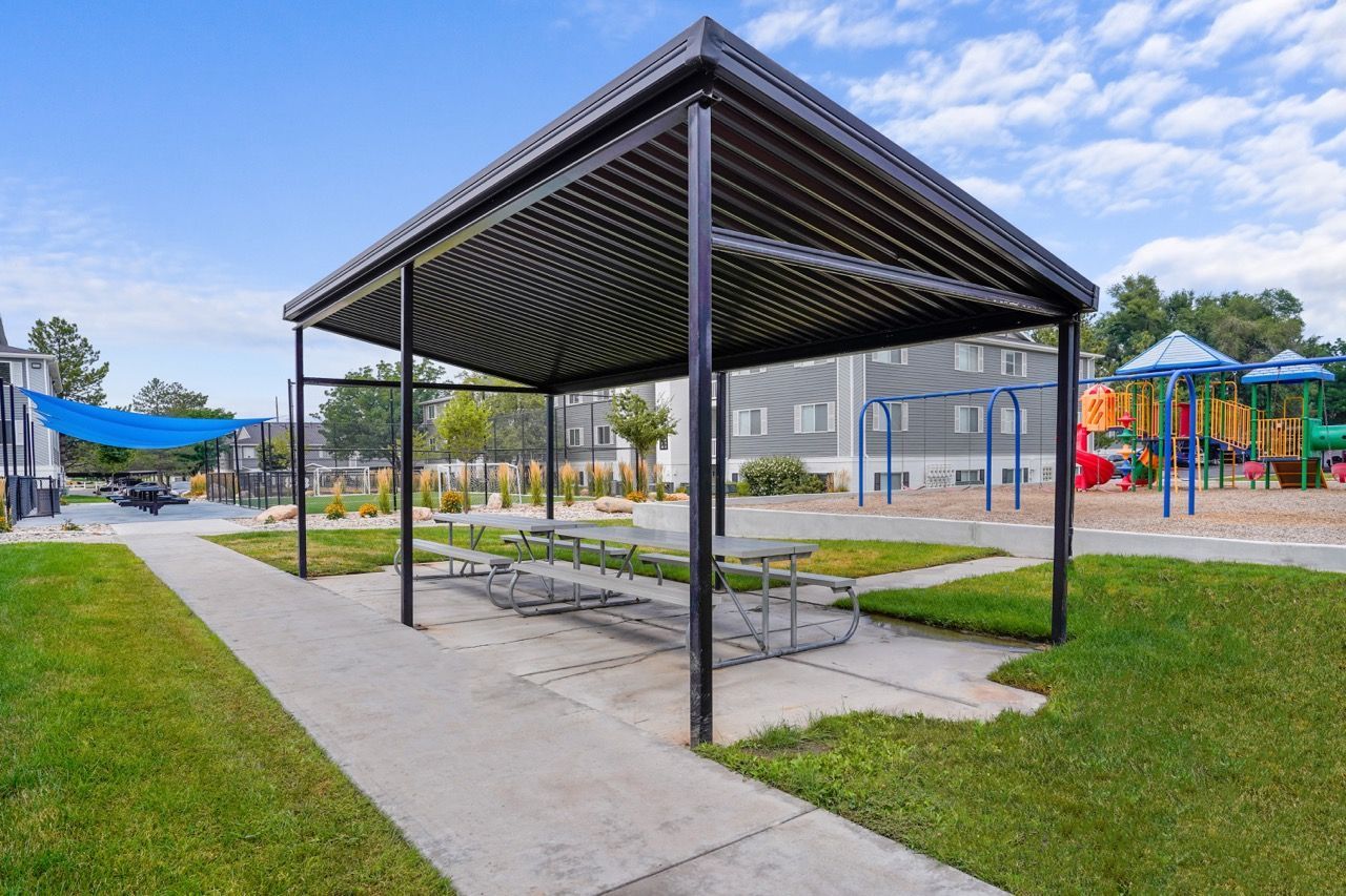 Covered picnic shelter with a table in a residential community; playground in the background.  Experience comfortable apartment living in Millcreek, UT, when you schedule a tour at Turnberry Apartments.

