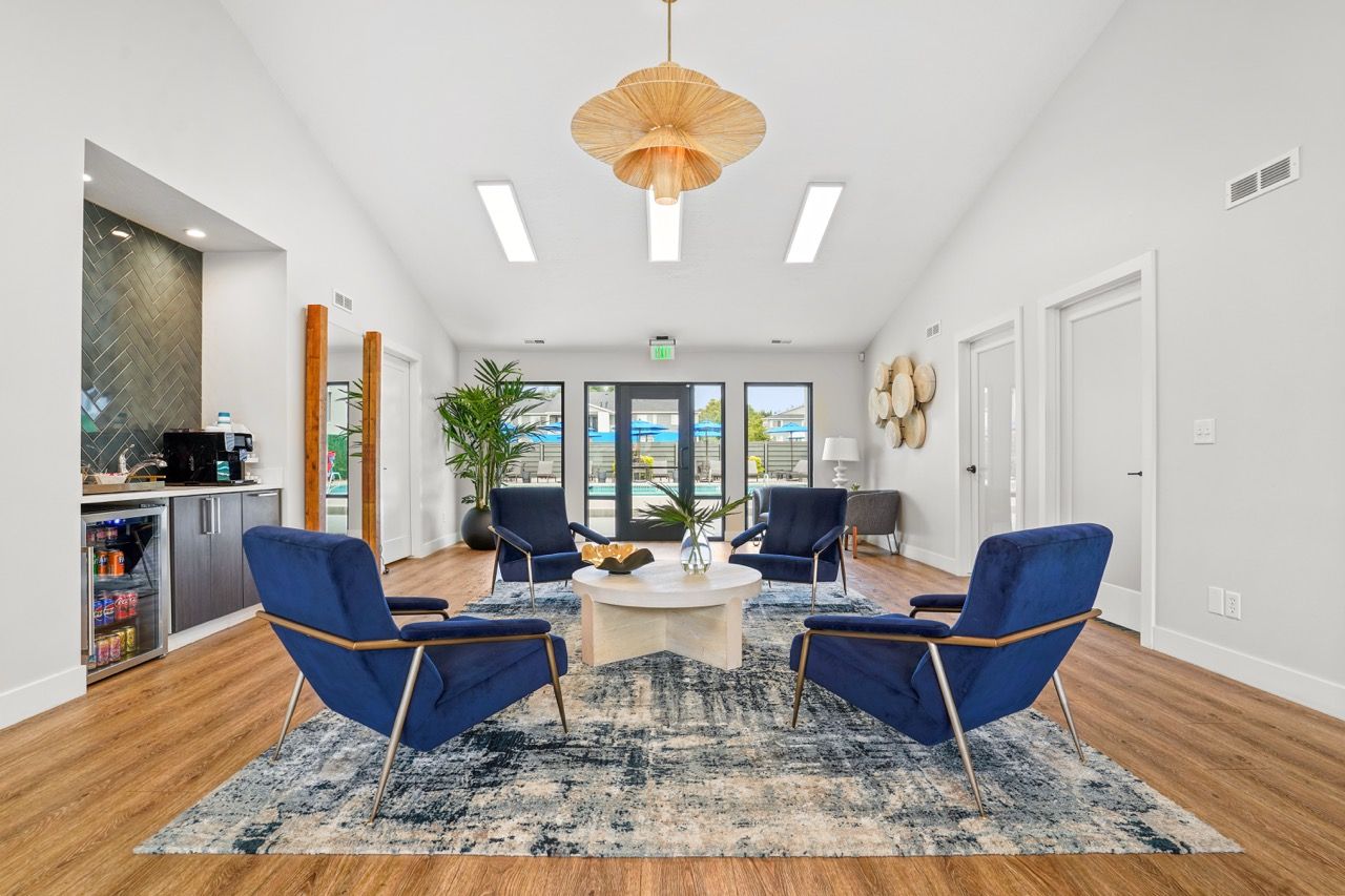Bright modern community lounge with blue chairs around a round table; pool area visible through glass doors.  Visit Turnberry Apartments to see our thoughtfully designed 1, 2 & 3 bedroom apartments in Millcreek, UT during a guided community tour.
