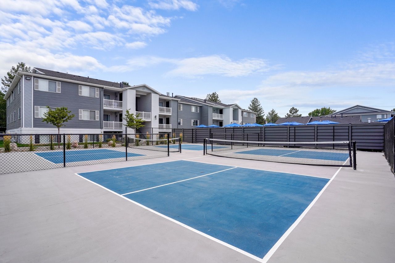 Exterior view of a multi-family community with blue tennis/pickleball courts and residential buildings.  Tour Turnberry Apartments to see welcoming pet-friendly townhomes in Millcreek, UT designed for everyday comfort.
