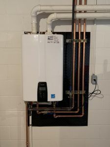 A white water heater is hanging on a wall next to copper pipes.