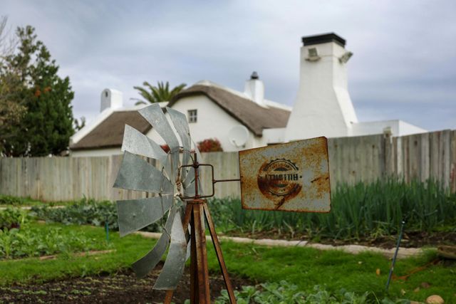A windmill in a garden with a house in the background