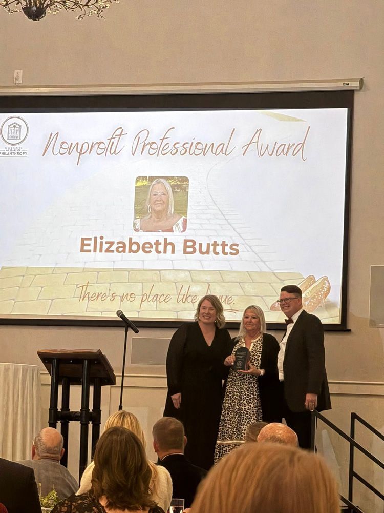 Woman Elizabeth Butts accepts award on stage. Screen says 