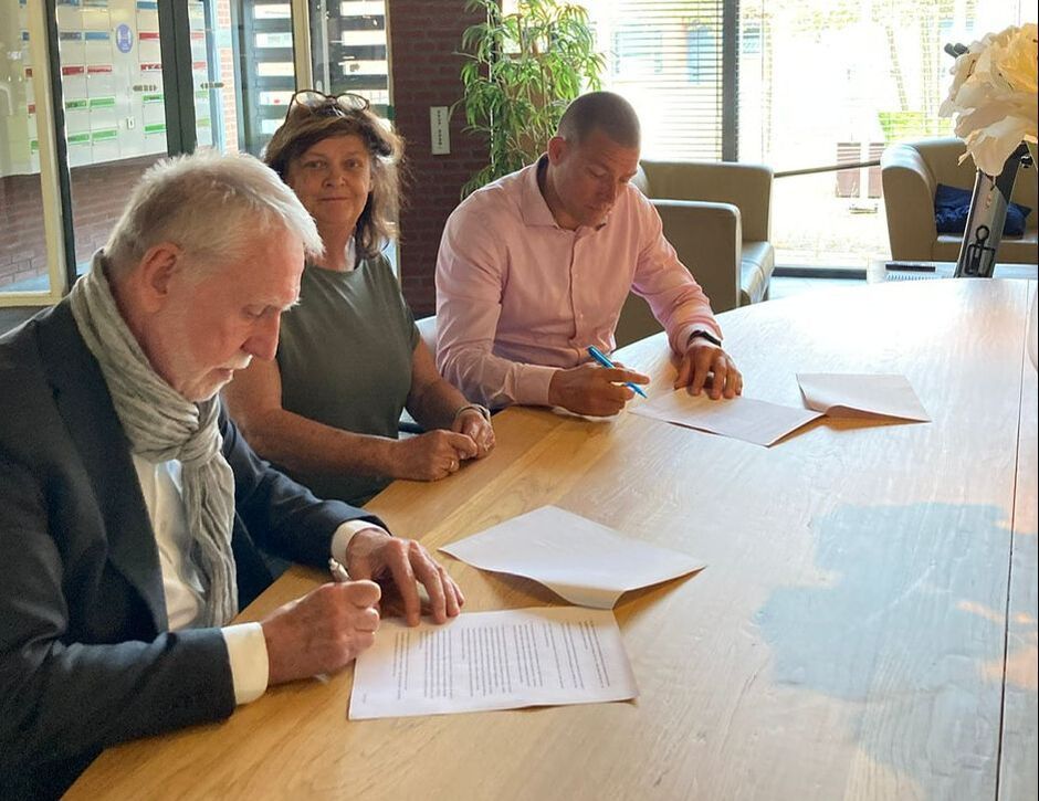 Drie mensen ondertekenen documenten aan een tafel; binnenopstelling.