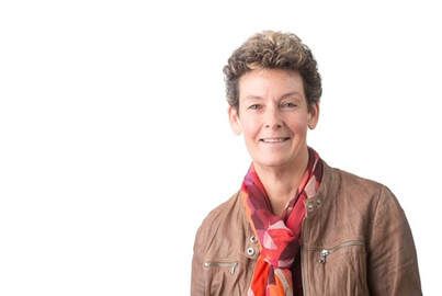 Vrouw met kort bruin haar, gekleed in een bruin jasje en een rode sjaal met print, glimlachend naar de camera.