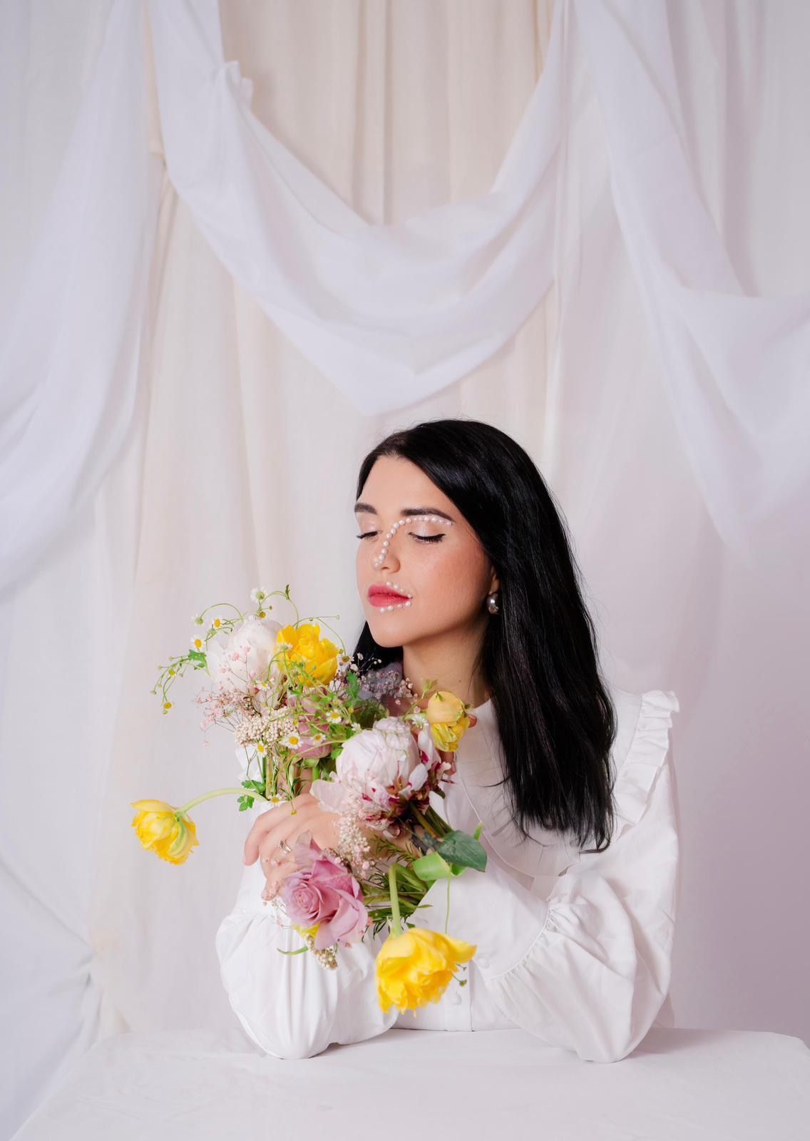 Una donna con i capelli scuri sorride, con le braccia incrociate e indossa un blazer scuro.