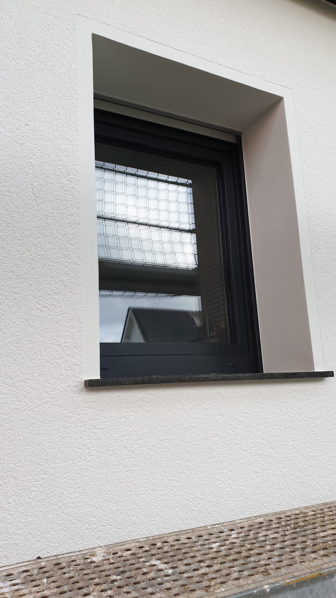 Fenster mit schwarzem Rahmen, grauer Verkleidung und weißer strukturierter Wand.