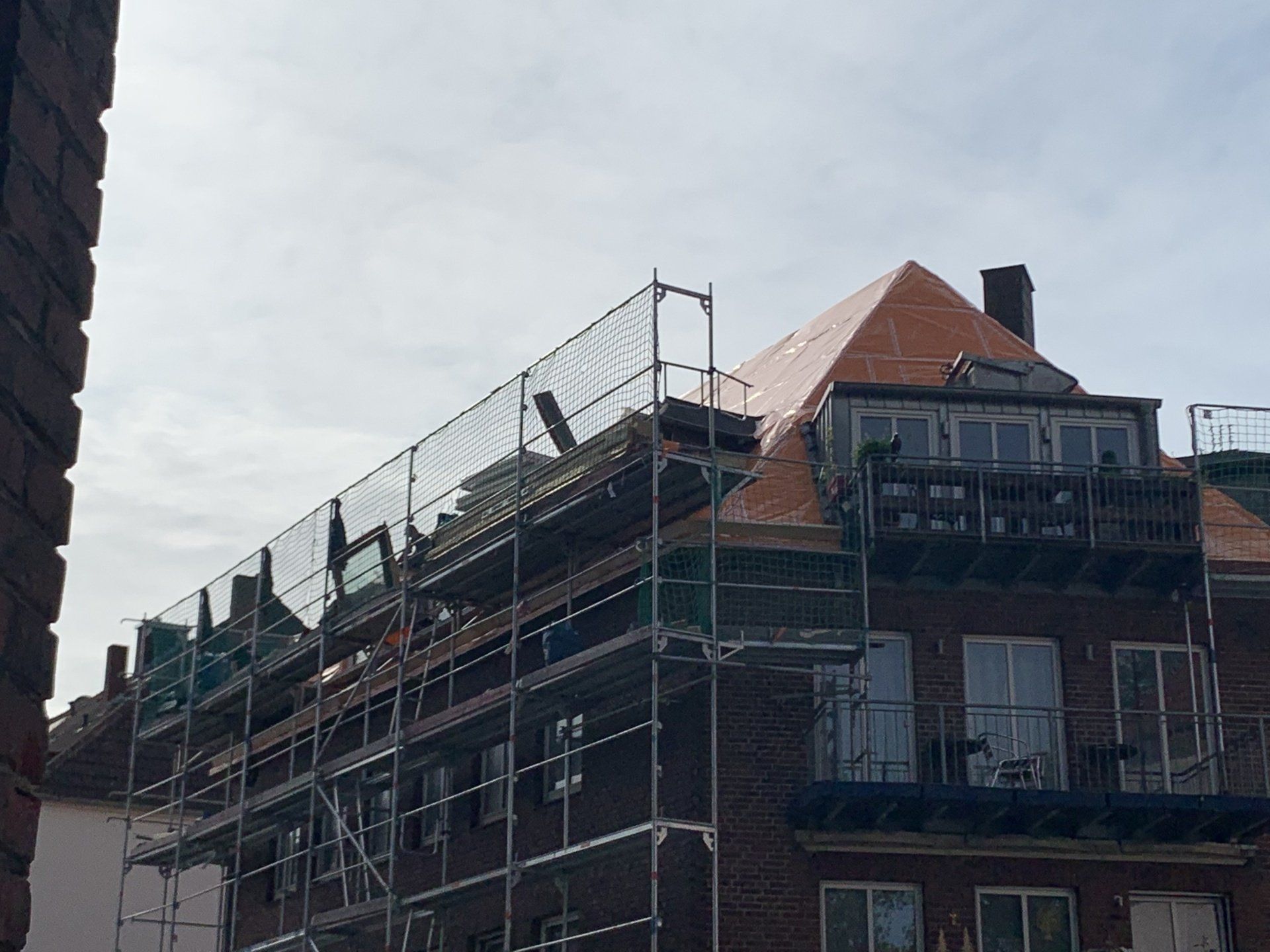 Gebäude im Bau, Gerüst mit Sicherheitsnetz, rotes Dach, Ziegelfassade.