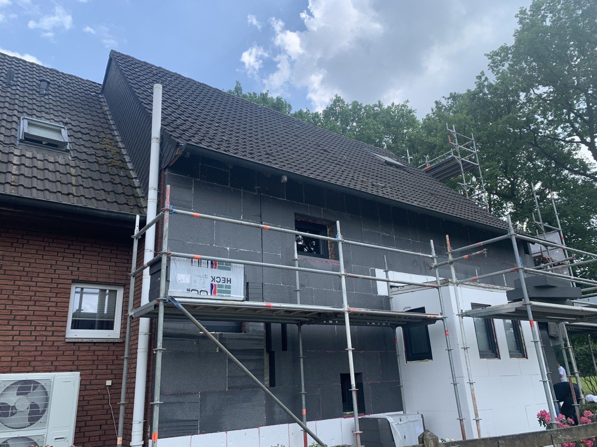 Außenansicht des Hauses wird renoviert; Gerüstumrandung, Dämmplatten an der Wand, Ziegel- und Schindeldach.
