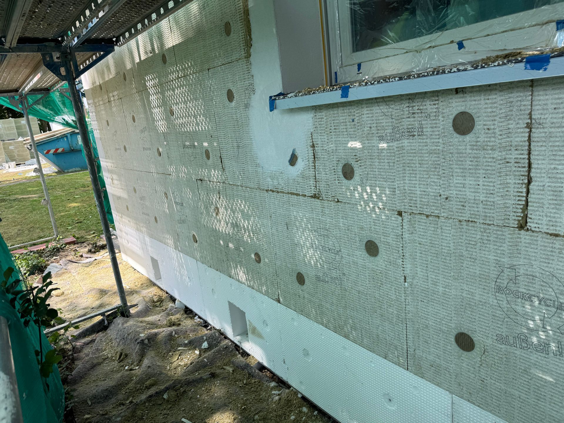 Außenwand im Bau mit Dämmplatten und Gerüst. Weiße und grüne Farbtöne.