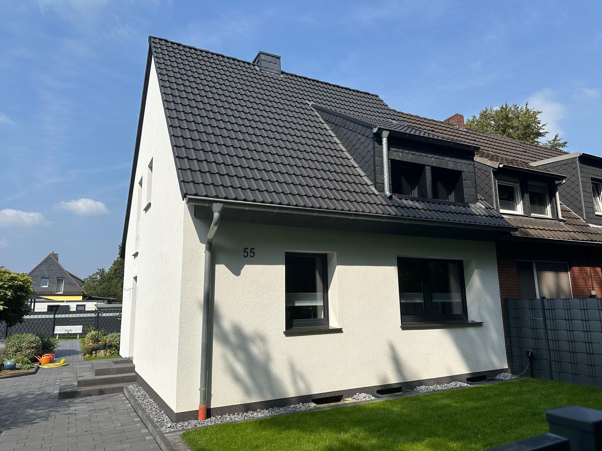 Weißes Haus mit dunkelgrauem Dach, schwarzen Fenstern und grünem Rasen.