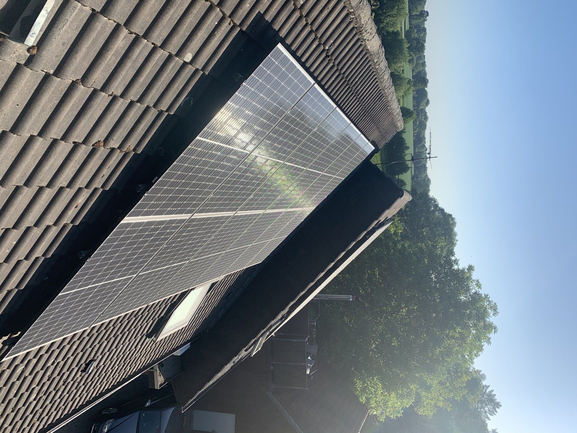 Auf einem Ziegeldach installierte Sonnenkollektoren. Heller, sonniger Tag mit viel Grün im Hintergrund.