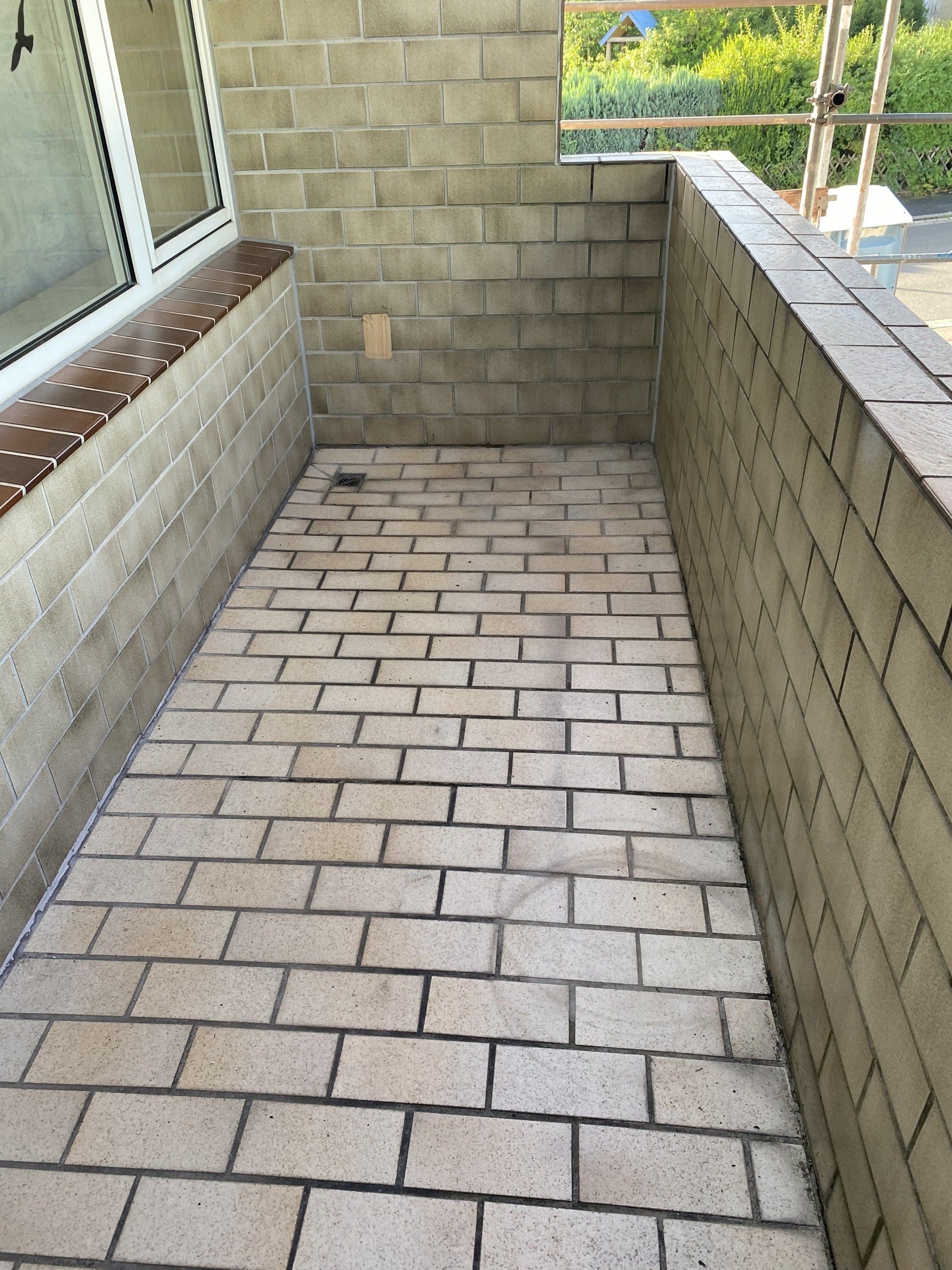 Im Bau befindlicher, rechteckiger Balkon mit Ziegelsteinpflaster, Wänden aus Schlackenblöcken und einem Fenster im Freien.