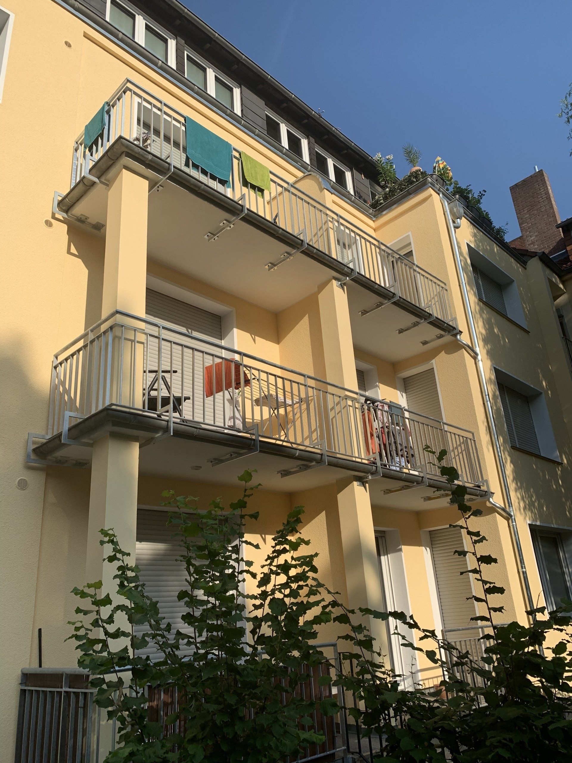 Gelbes Wohnhaus mit Balkonen, geschmückt mit Pflanzen und Möbeln.