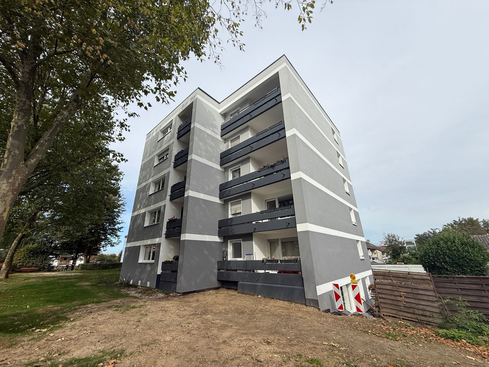 Graues Mehrfamilienhaus mit dunklen Balkonen an einem bewölkten Tag.