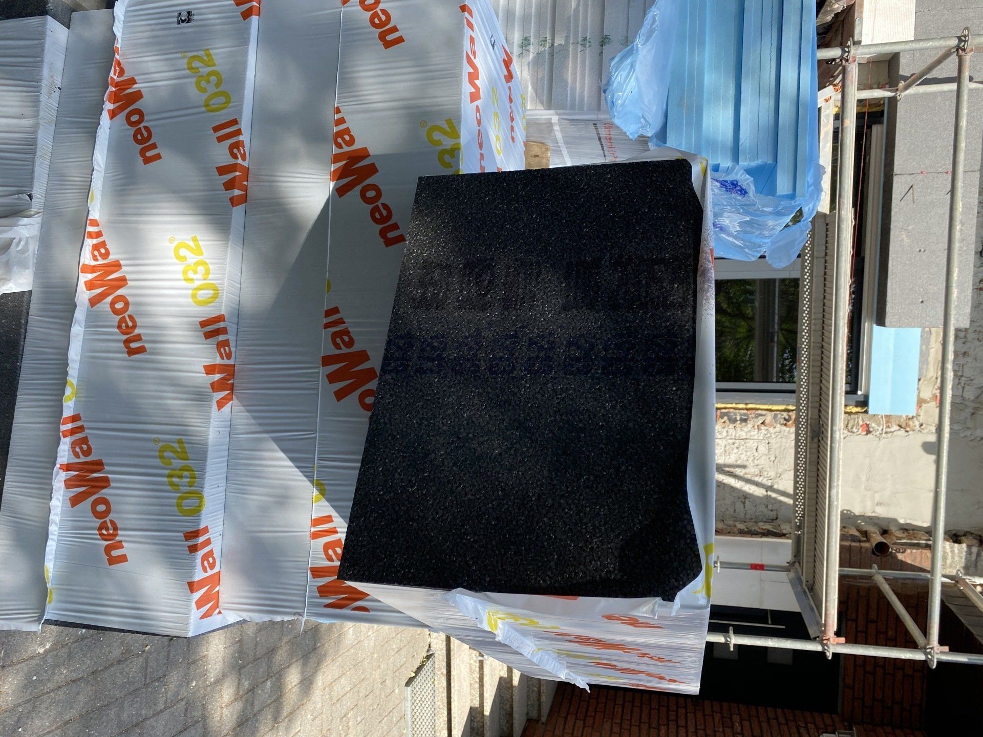 Schwarze Dämmplatte auf verpackter Wanddämmung mit Gerüst.