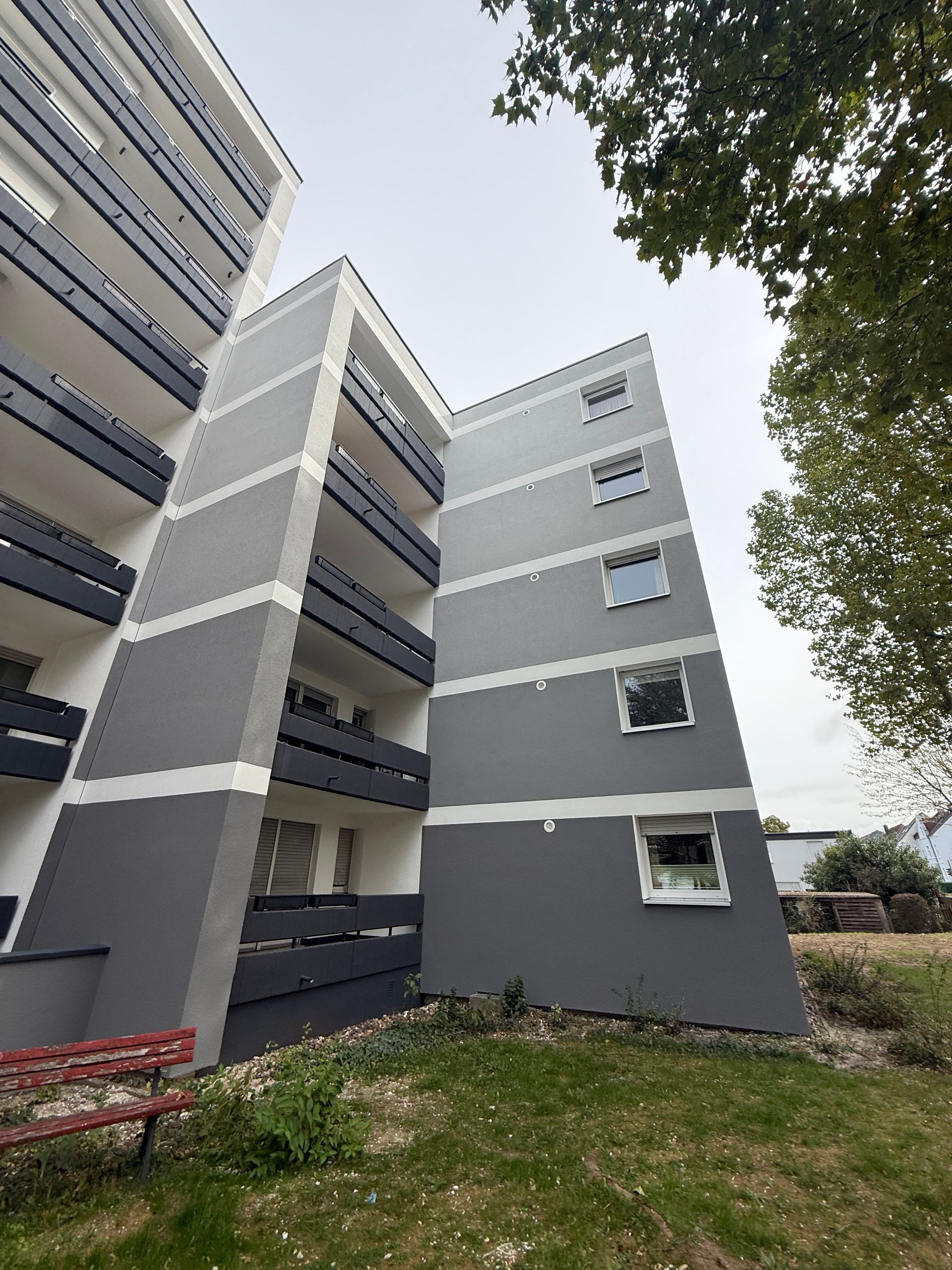 Graues Mehrfamilienhaus mit Balkonen unter bewölktem Himmel.