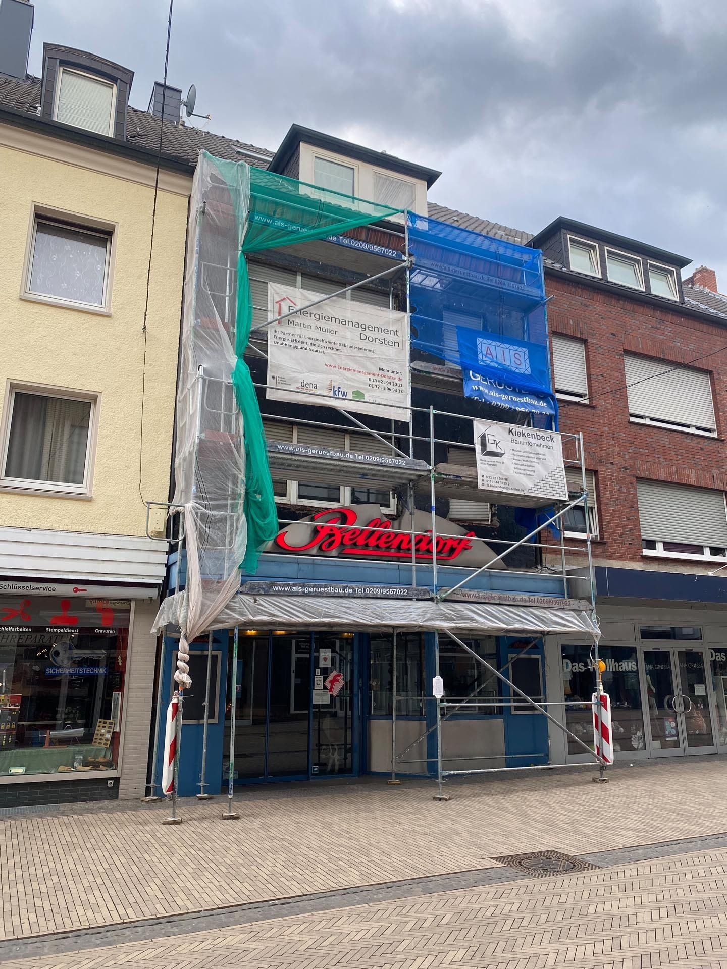 Gebäude mit Gerüst und Schutznetz; Ladenschild sichtbar.