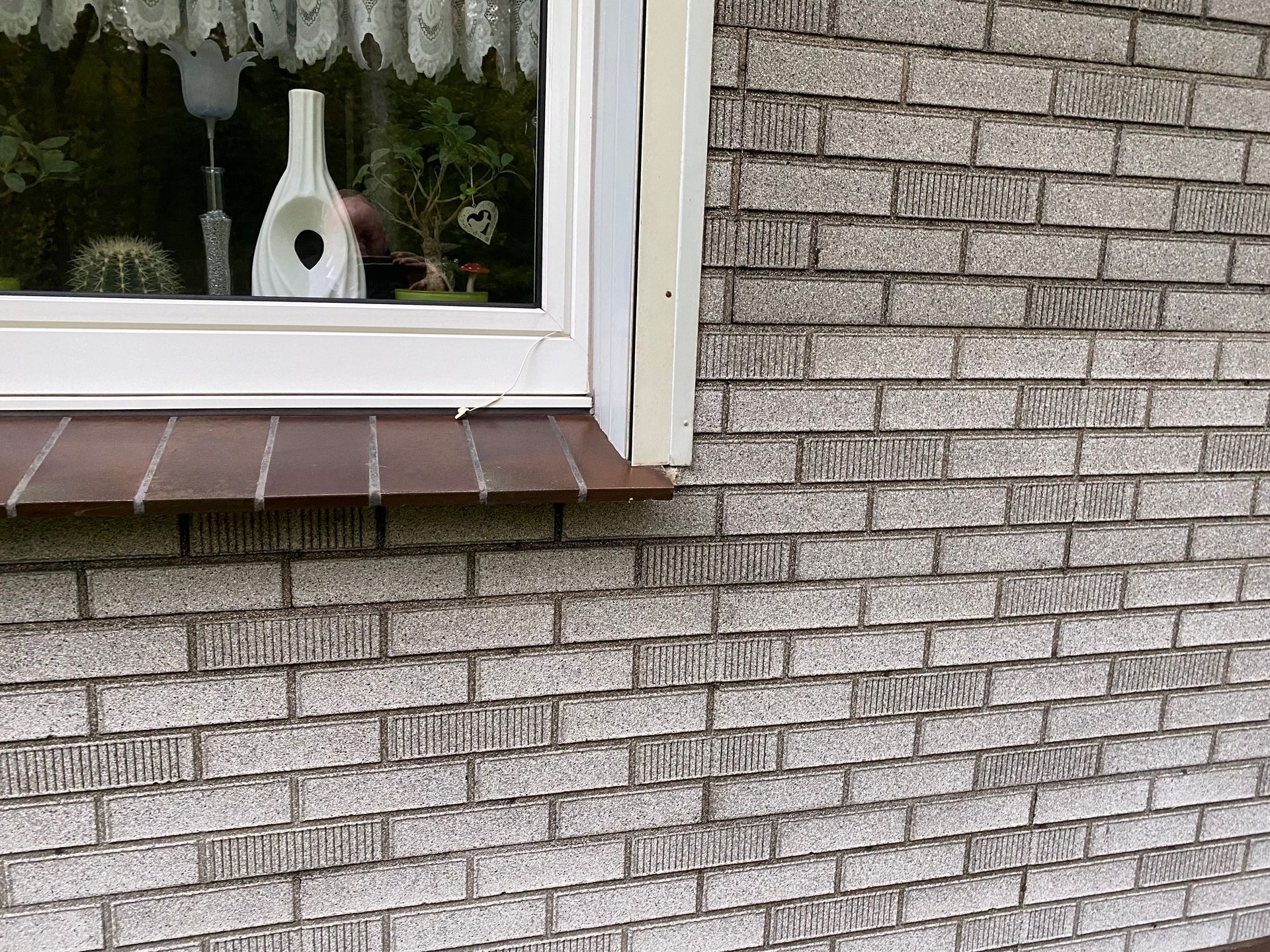 Außenwand aus Ziegeln neben einem Fenster mit brauner Fensterbank.