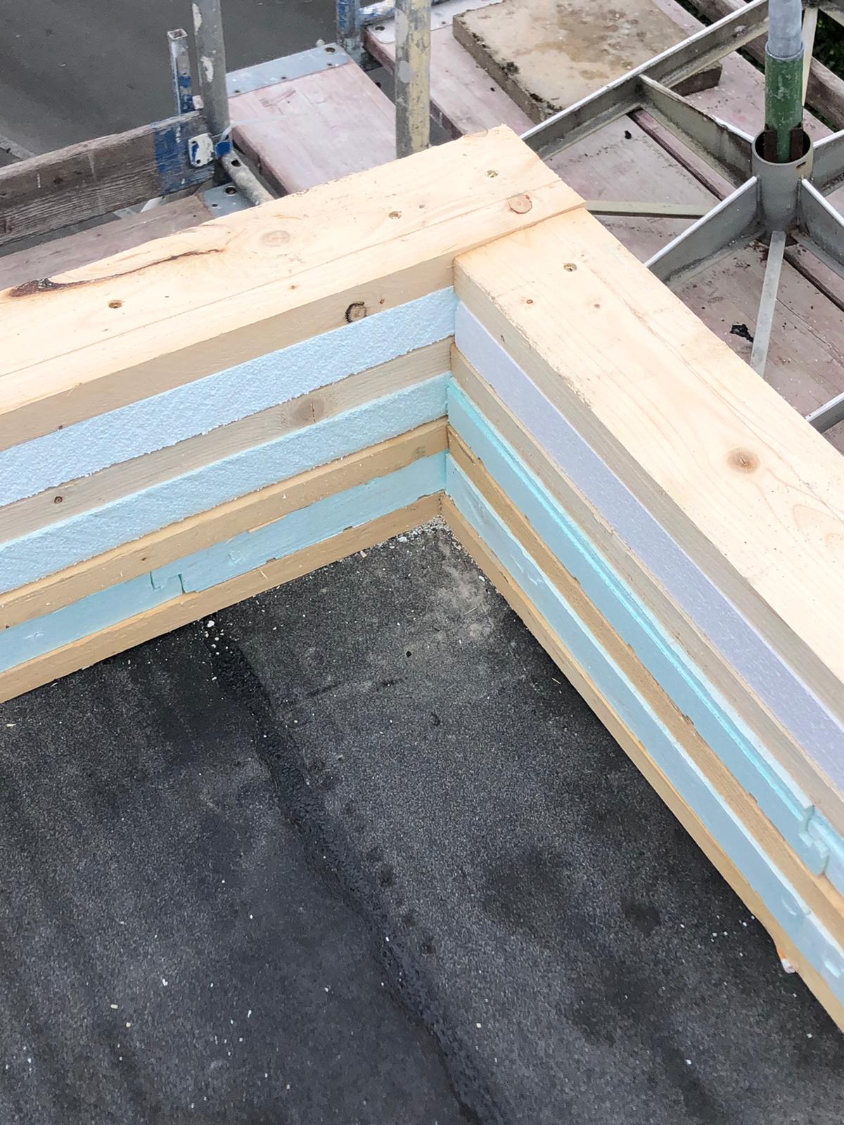Ecke eines im Bau befindlichen Gebäudes mit Holzrahmen und blau-weißer Isolierung.