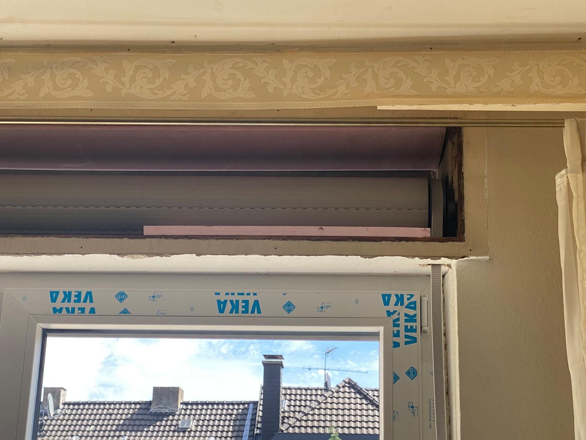 Fenster mit teilweise geöffnetem Rollladen, der die Isolierung im darüber liegenden Raum zeigt.