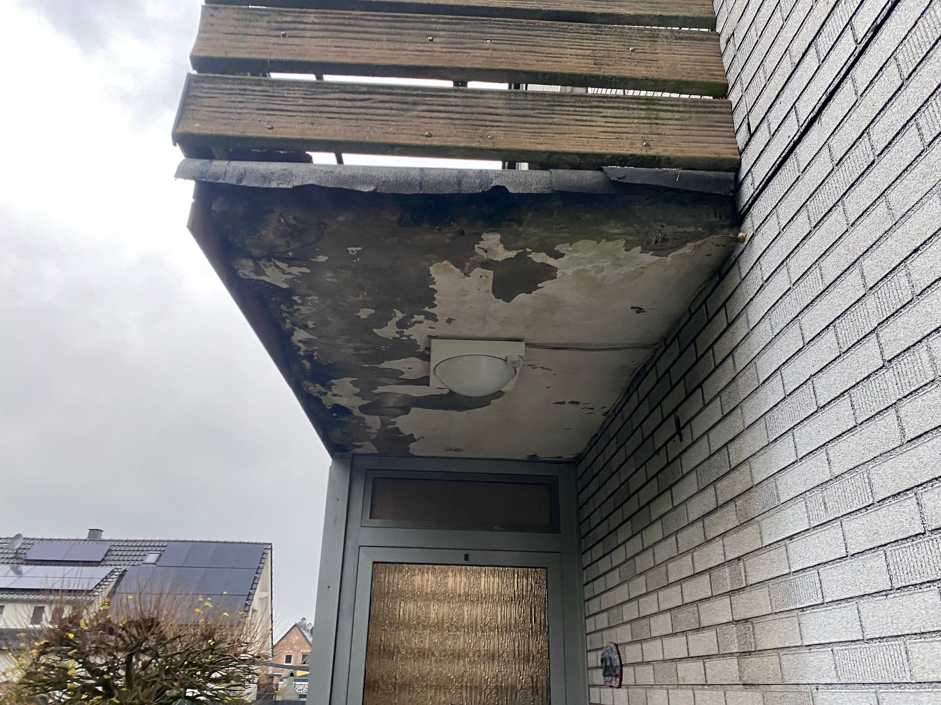 Balkon mit abblätternder Farbe und verwittertem Holzgeländer an einem Backsteingebäude.