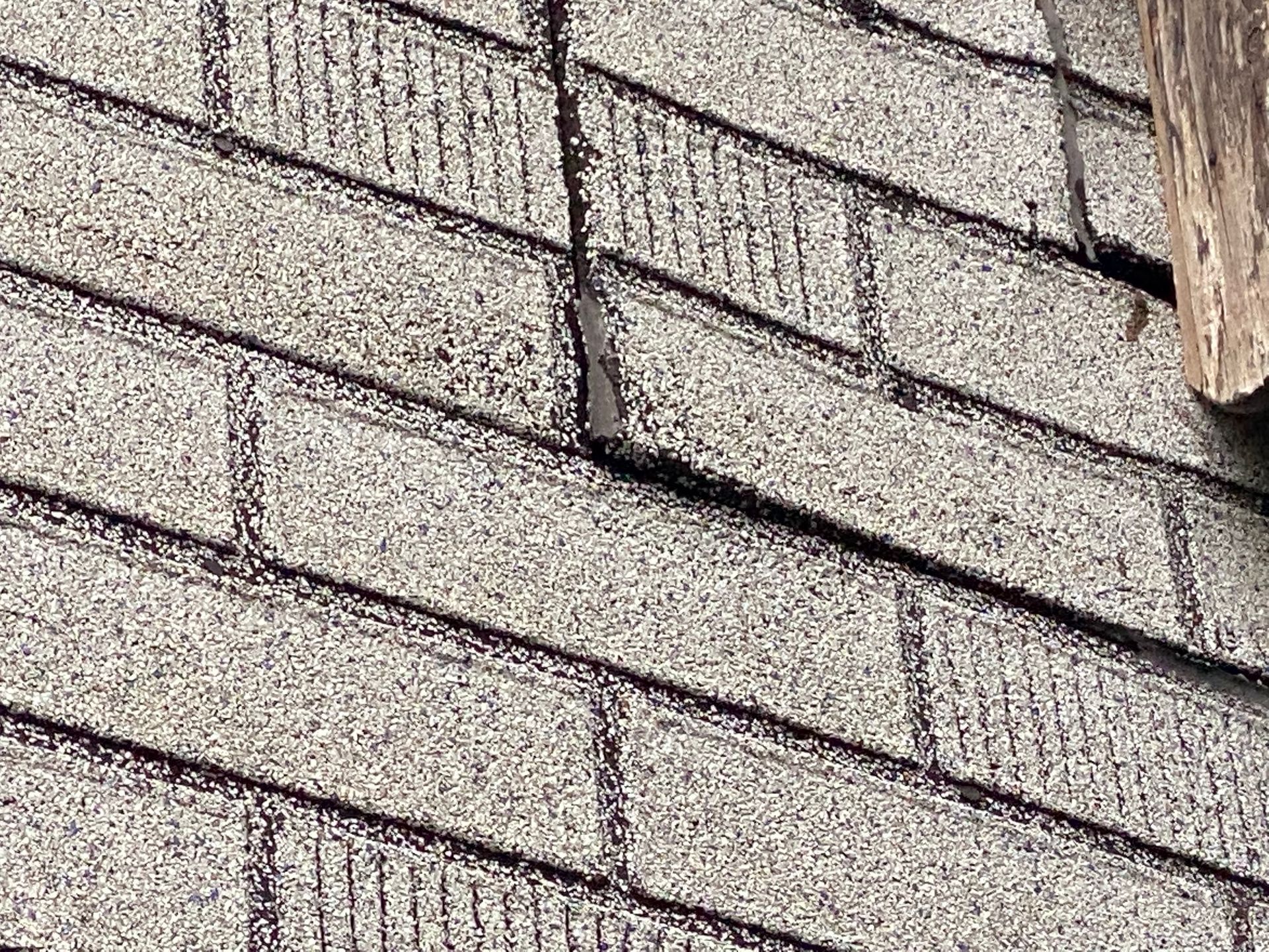 Nahaufnahme eines grauen Asphaltschindeldachs mit einem vertikalen Riss.